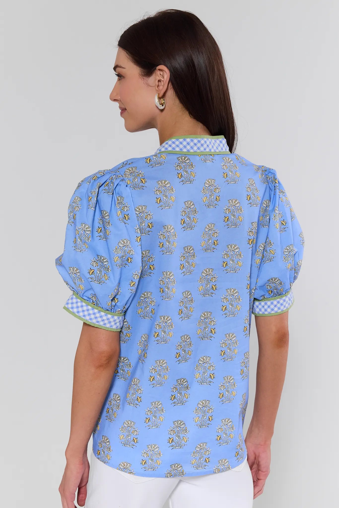 Woman wearing a blue patterned blouse with checkered trim on a plain background