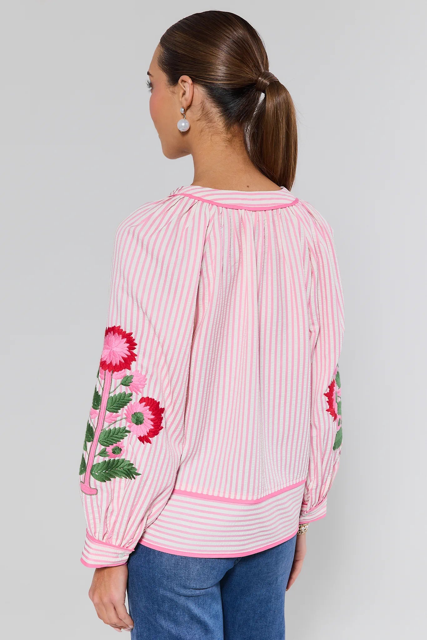 Woman wearing a pink and white striped blouse with floral embroidery on a plain background