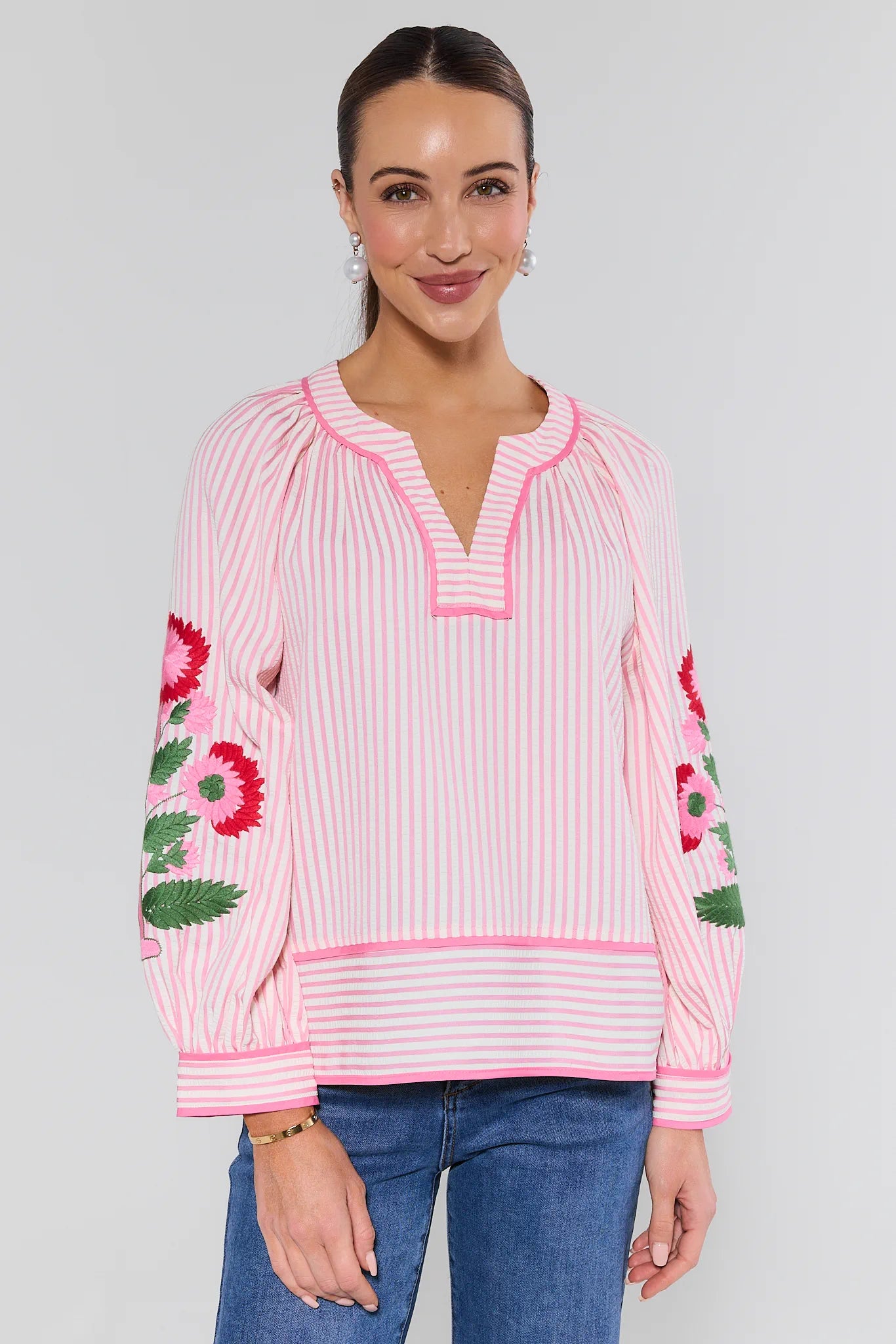 Woman wearing a pink and white striped blouse with floral embroidery on a plain background