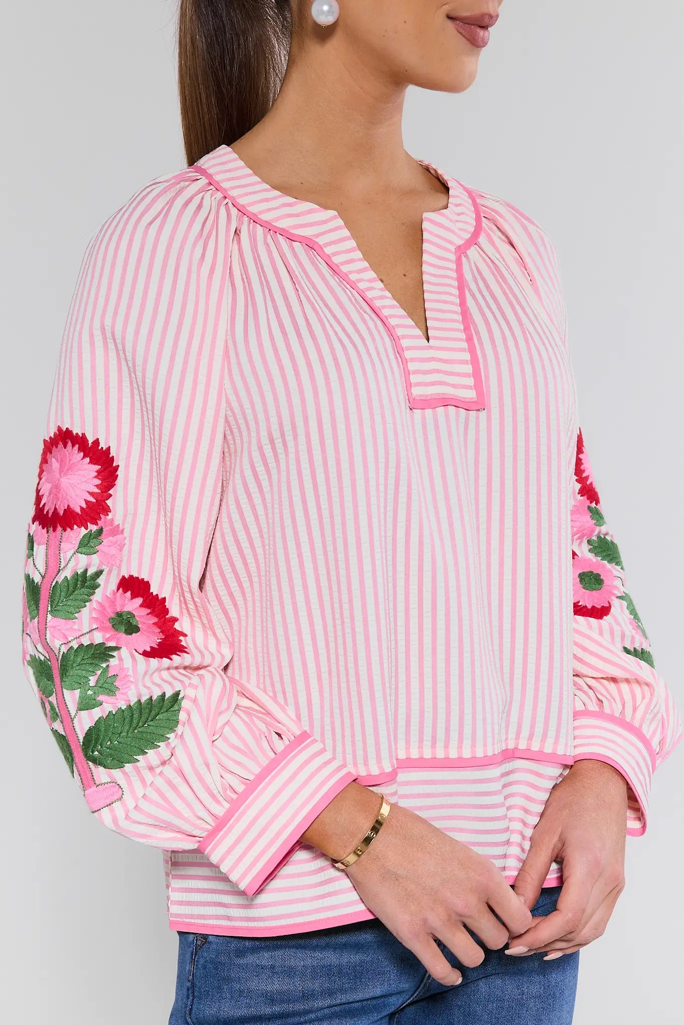 Pink and white striped blouse with floral cuffs on a plain background