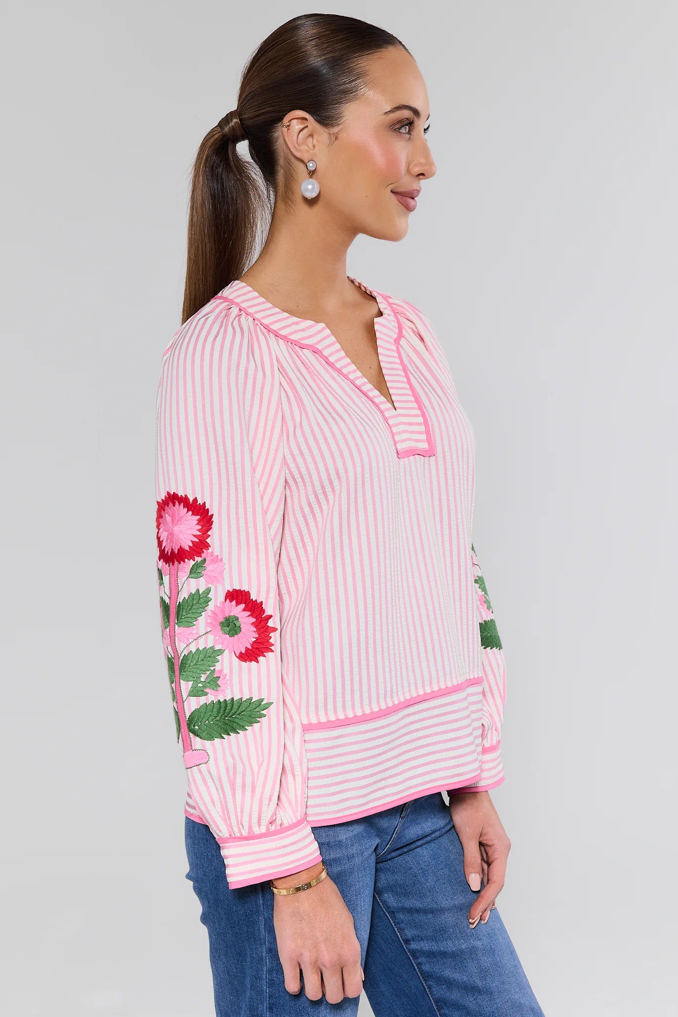 Woman wearing a pink striped blouse with floral embroidery on a gray background