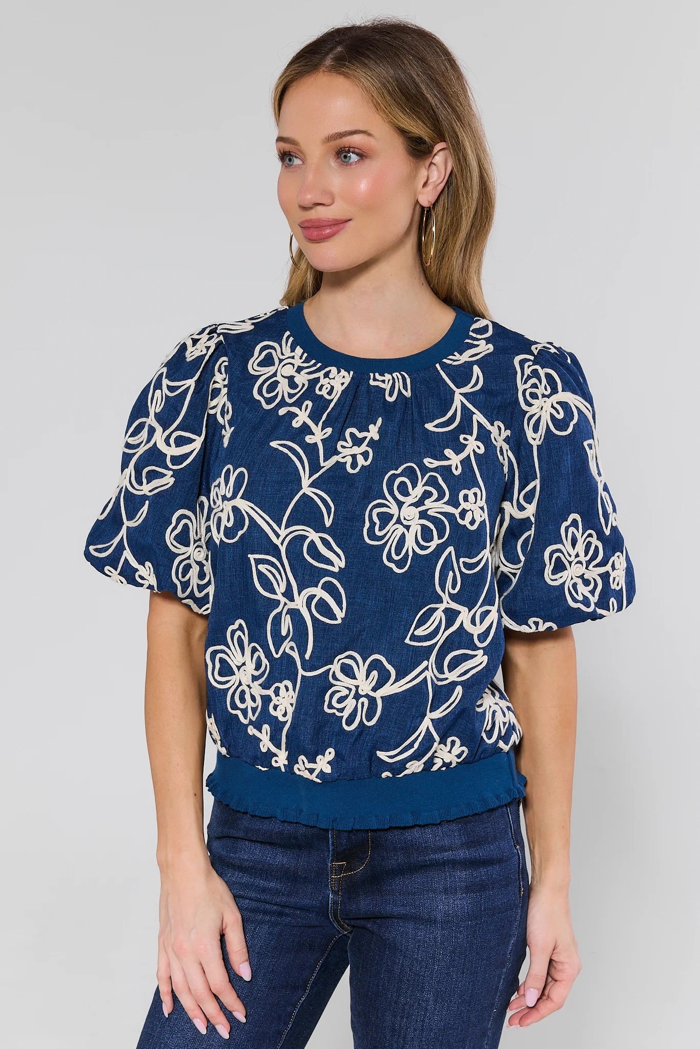 woman wearing navy embroidered top with jeans on a white background