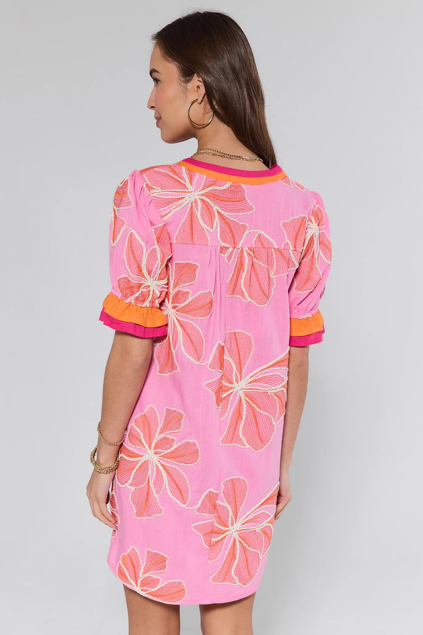 Woman wearing a pink floral dress with orange accents on a plain background