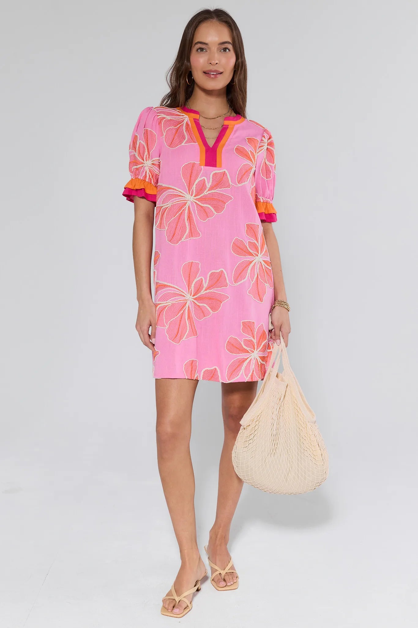 Woman wearing a pink floral dress holding a beige bag on a white background