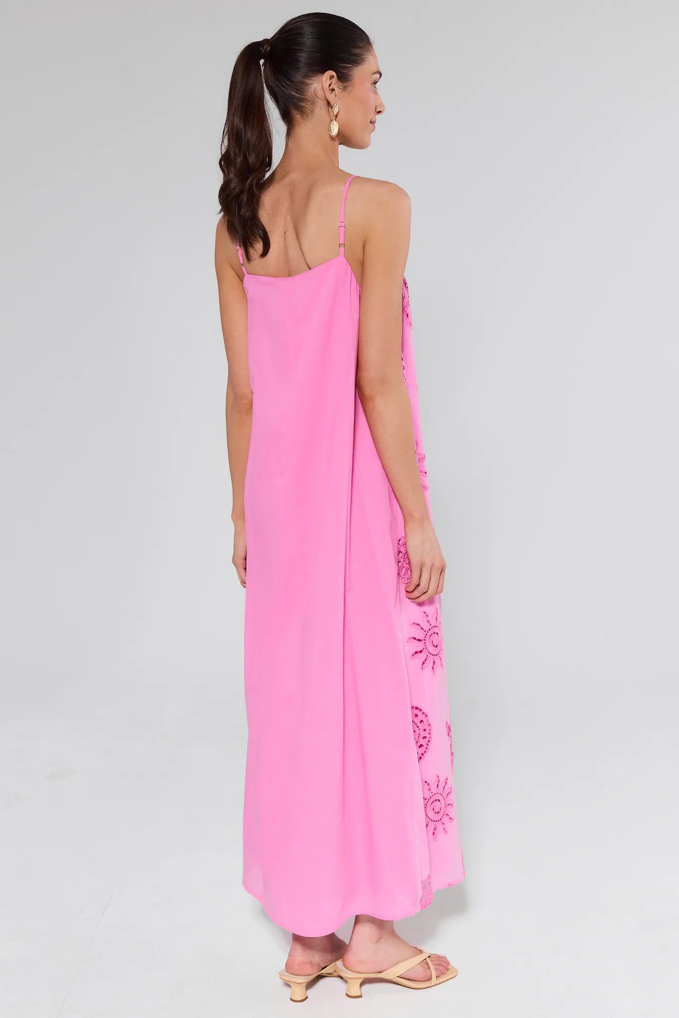 Woman wearing a pink slip dress with floral embroidery on a plain background