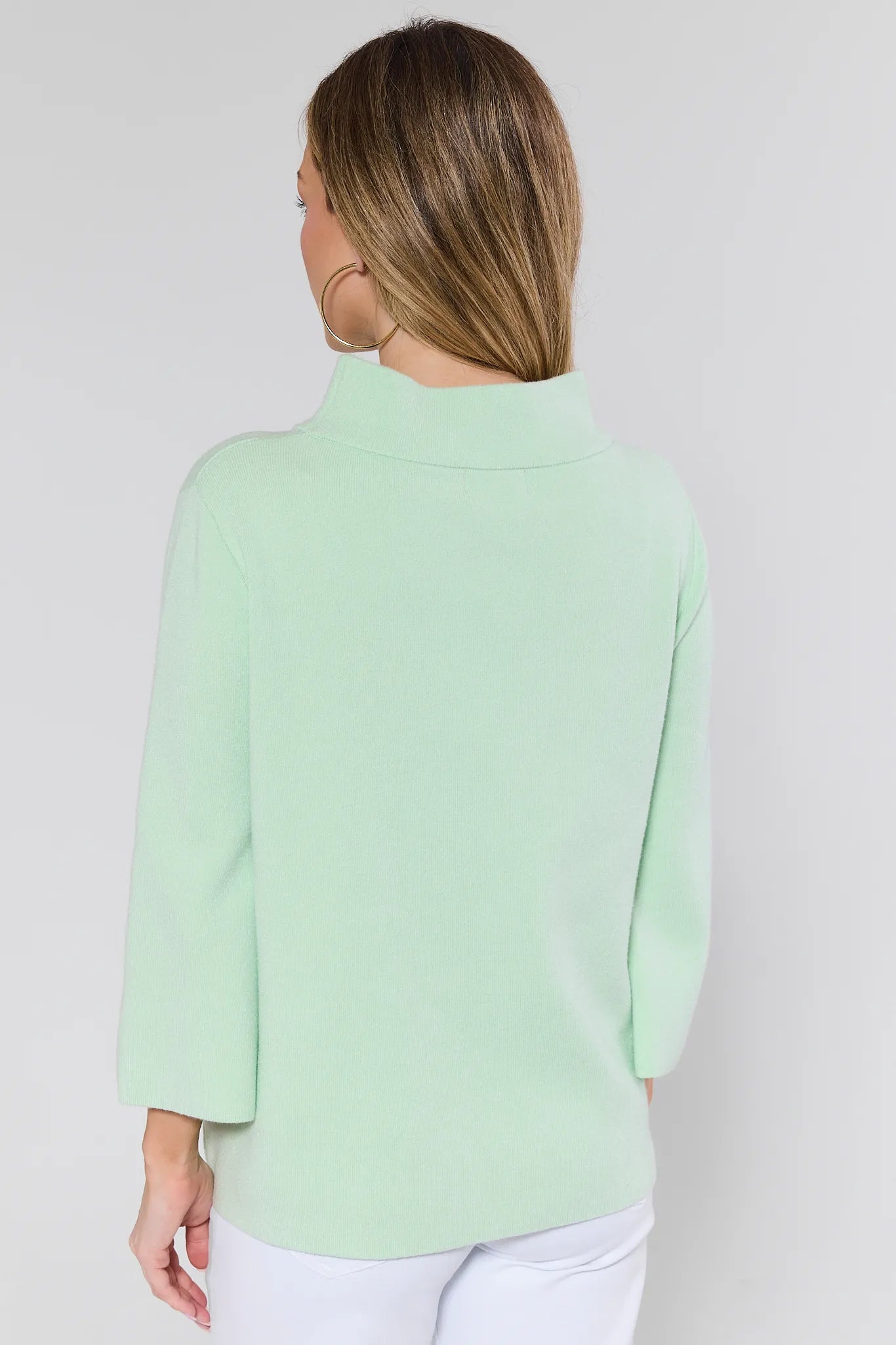 person wearing light green jackie sweater and white jeans on a white background