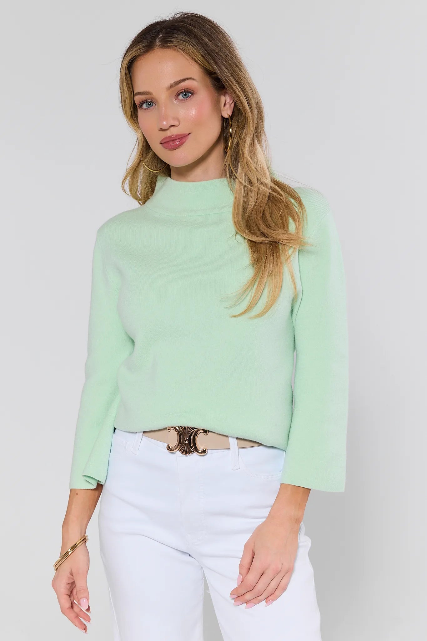 woman wearing light green jackie sweater and white jeans on a white background