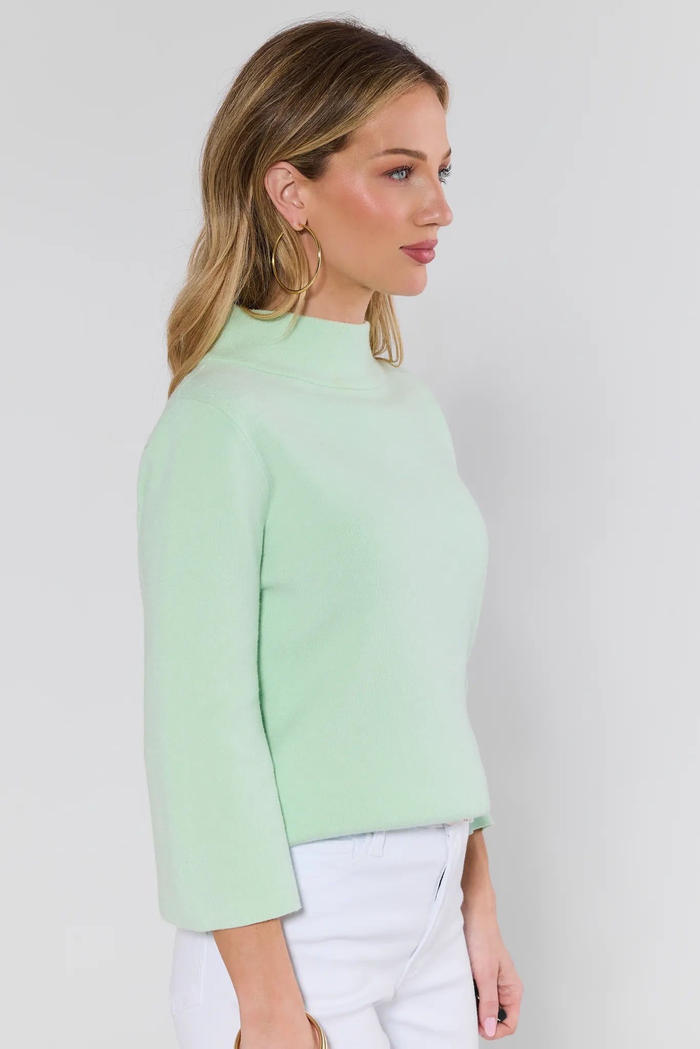 woman wearing light green jackie sweater and jeans on a white background