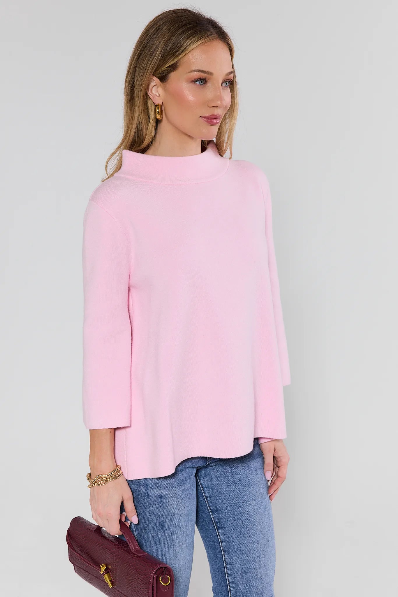 woman wearing light pink sweater and bag on white background
