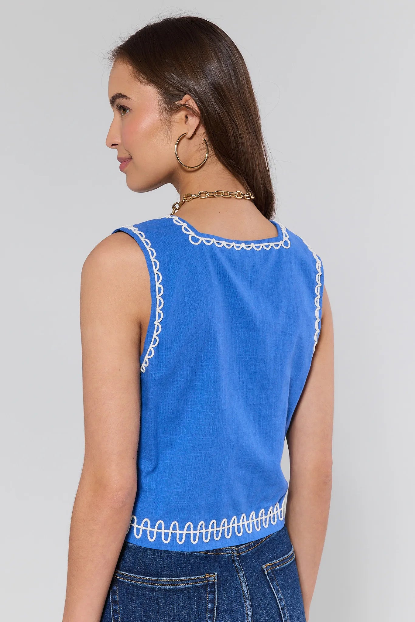 Woman wearing a blue sleeveless top with white trim on a plain background
