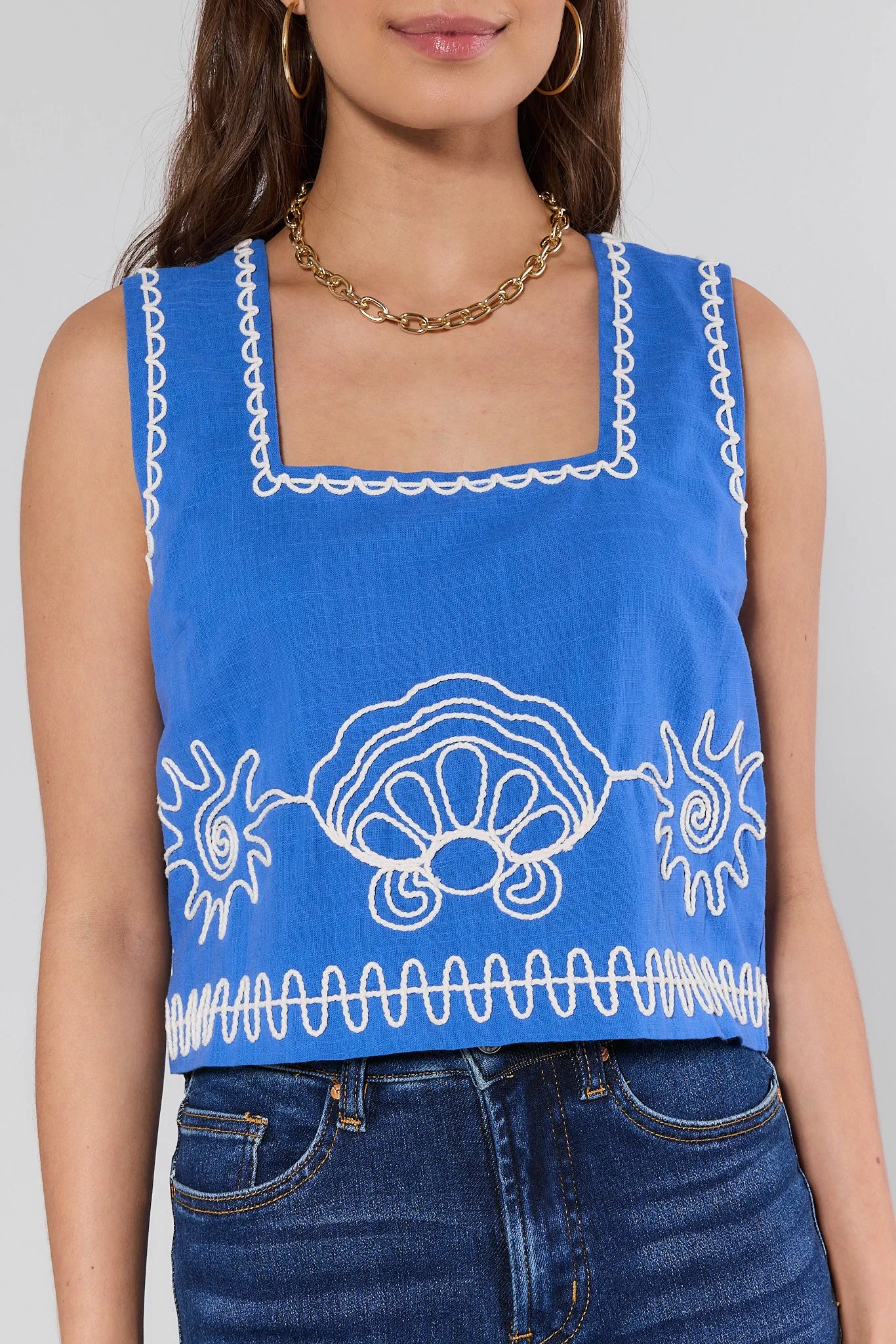Blue sleeveless top with white patterns worn by a person on a gray background