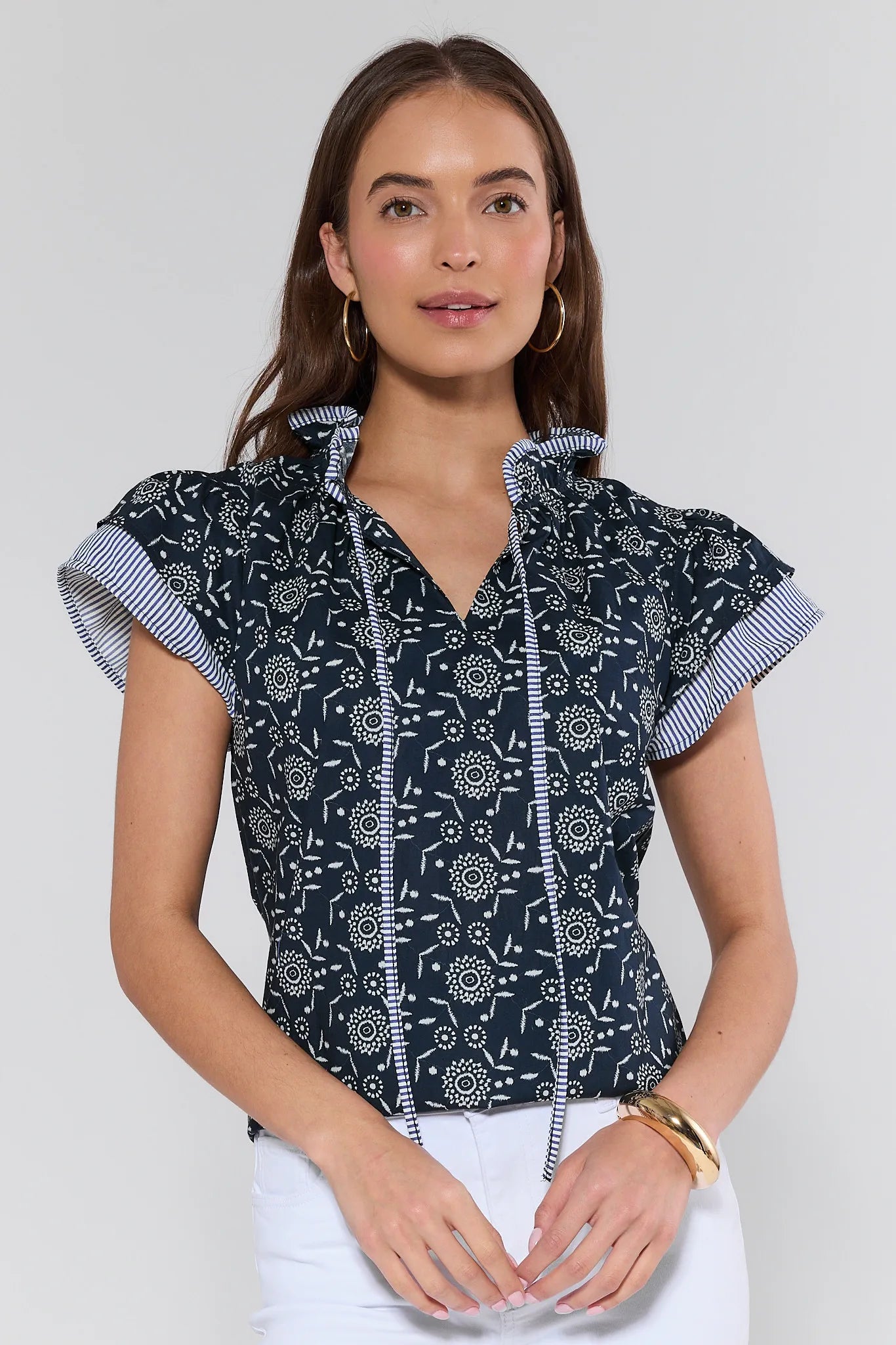 Woman wearing a navy blue patterned blouse with white pants on a light gray background