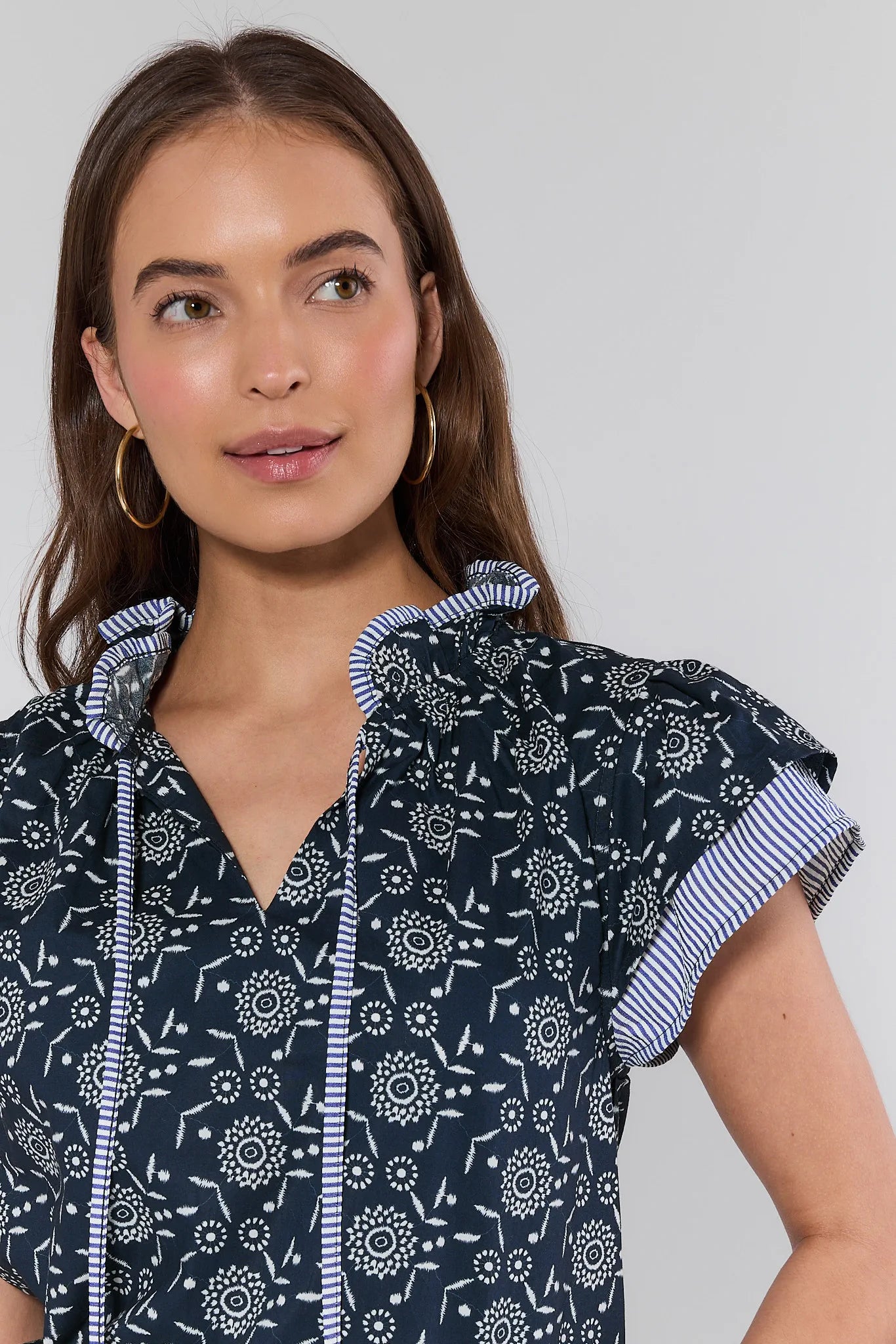 Woman wearing a navy floral dress with white ruffled sleeves against a gray background