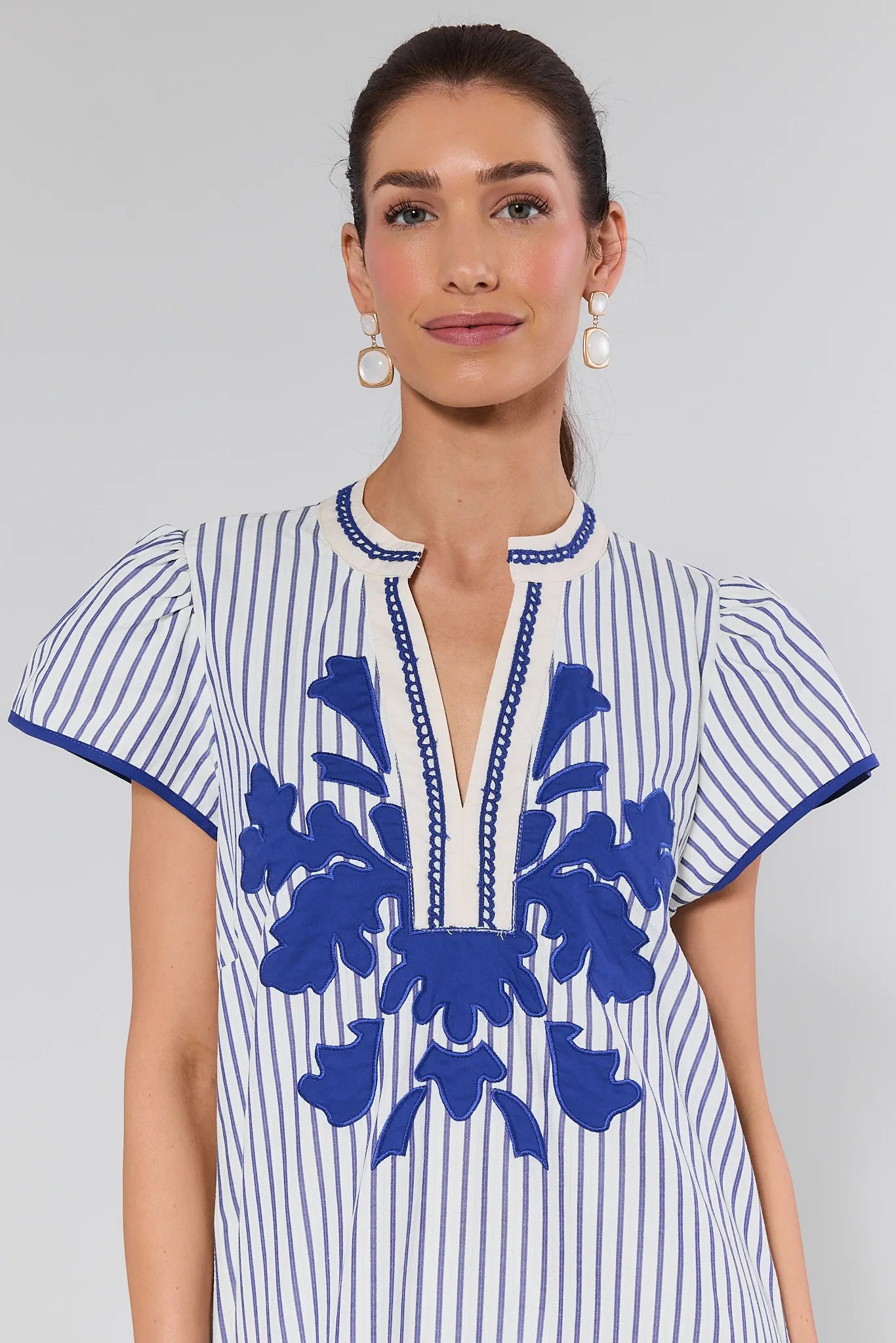 Woman wearing a white dress with blue floral embroidery on a plain background