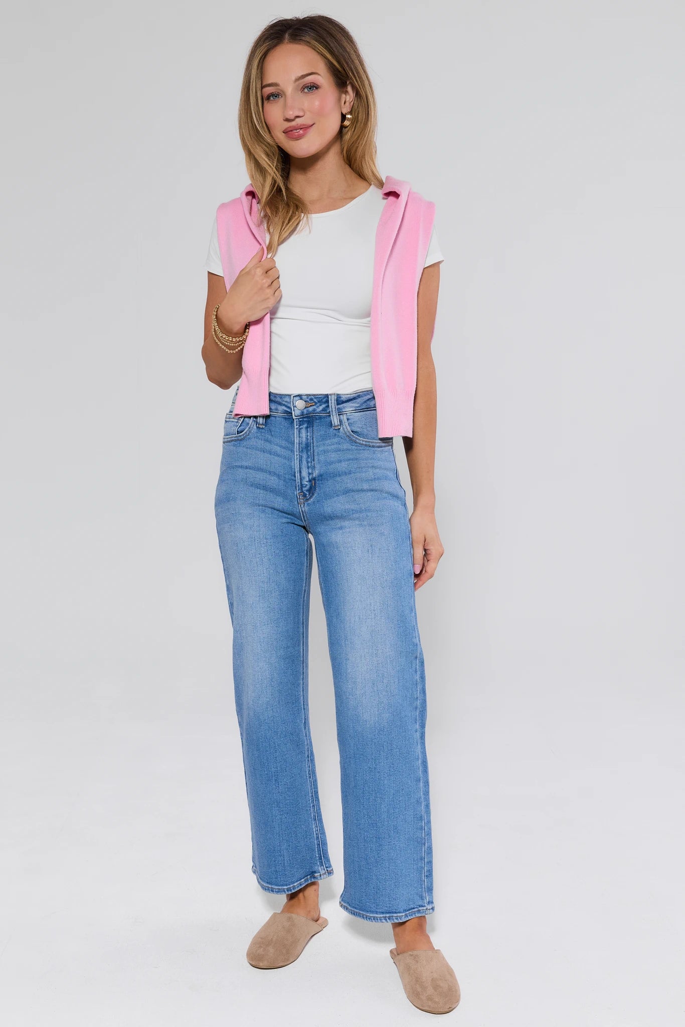 Woman wearing a pink jacket, white shirt, and blue jeans on a plain background