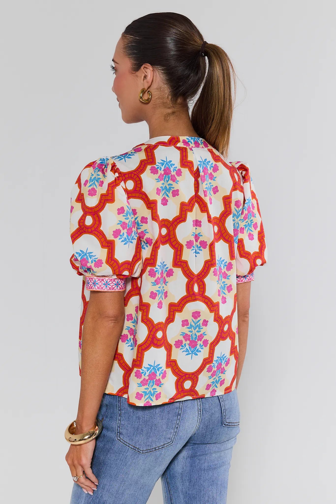 Woman wearing a colorful patterned blouse with blue jeans on a plain background