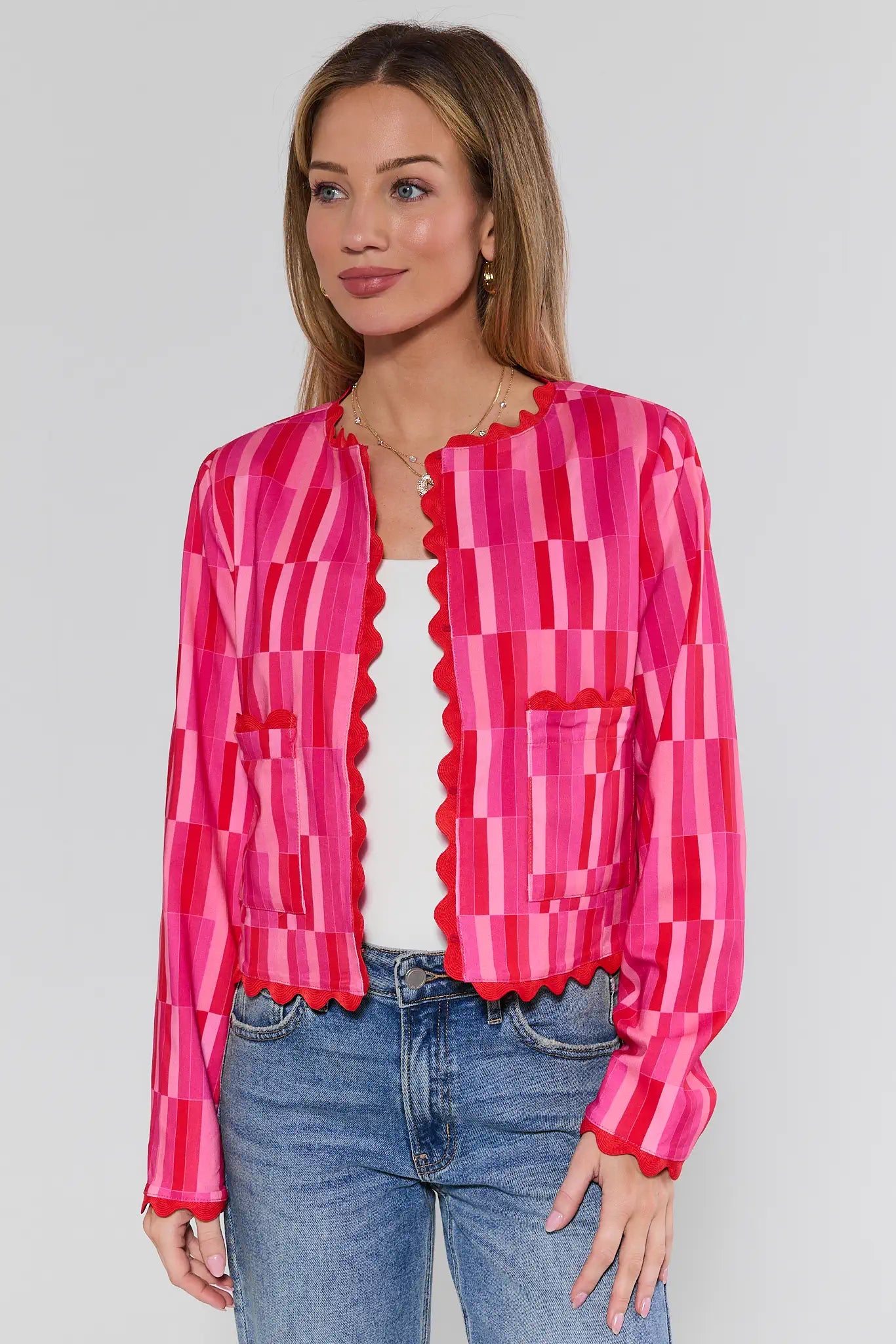 Woman wearing a bright pink and red patterned blouse with blue jeans on a plain background