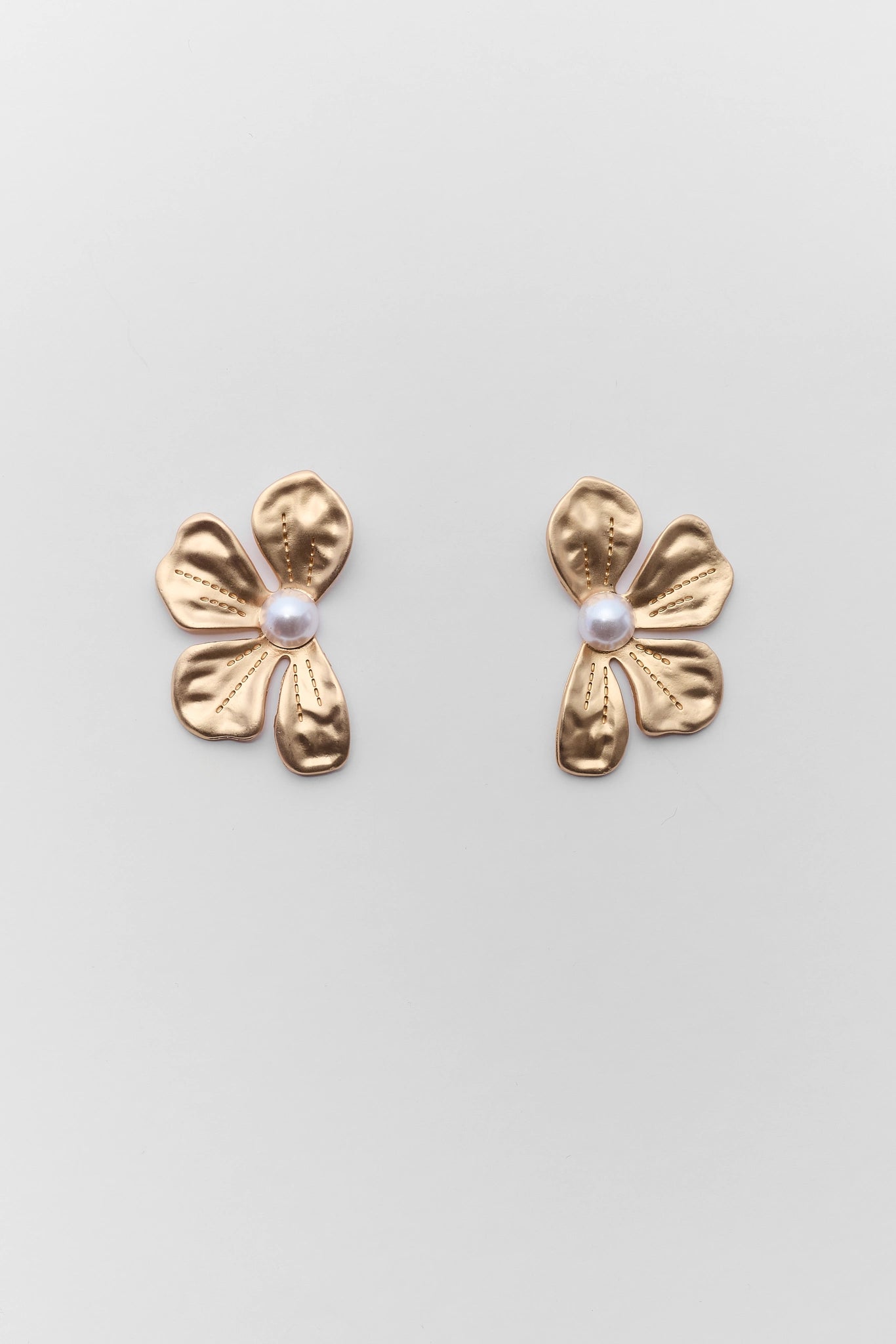 Gold flower-shaped earrings with pearl centers on a light gray background
