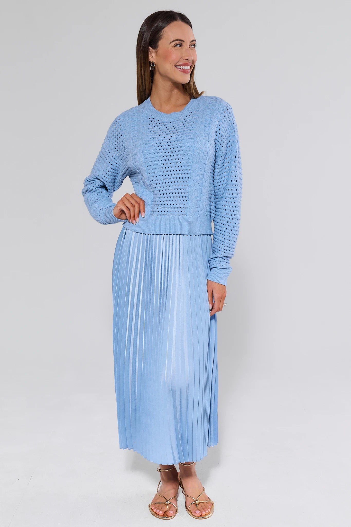 Woman wearing a light blue textured top and pleated skirt on a white background