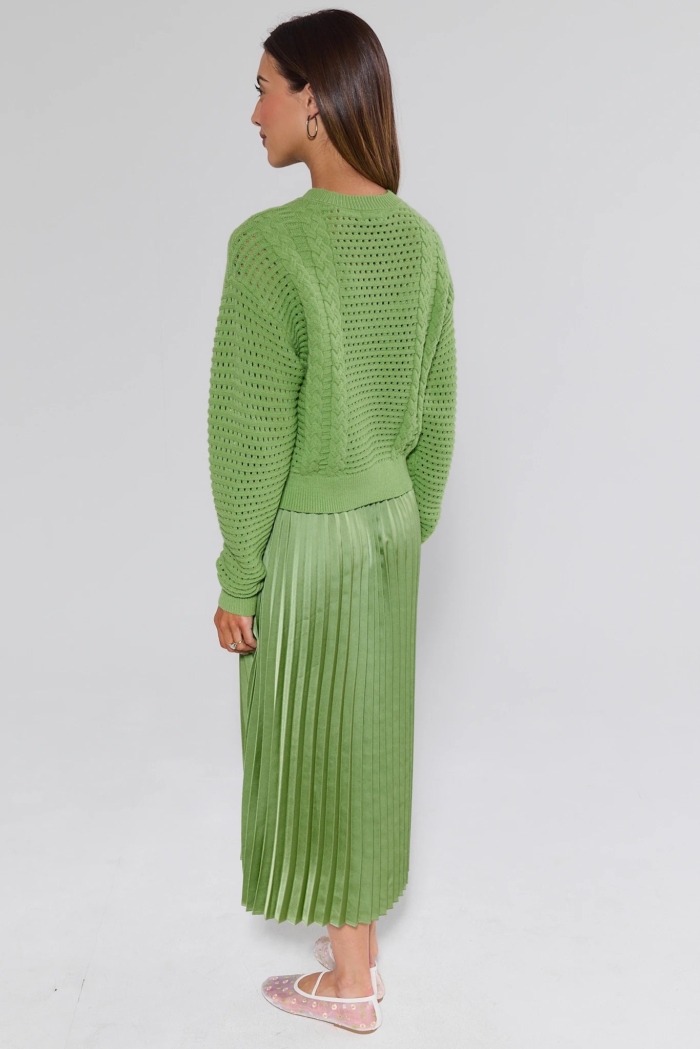 Woman wearing a green textured sweater and pleated skirt on a white background