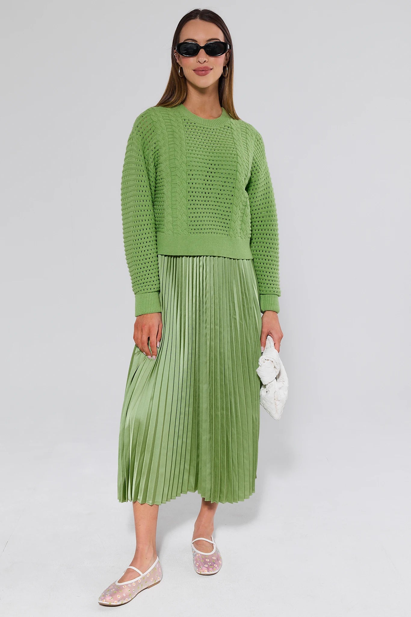 Woman wearing a green sweater and pleated skirt on a white background