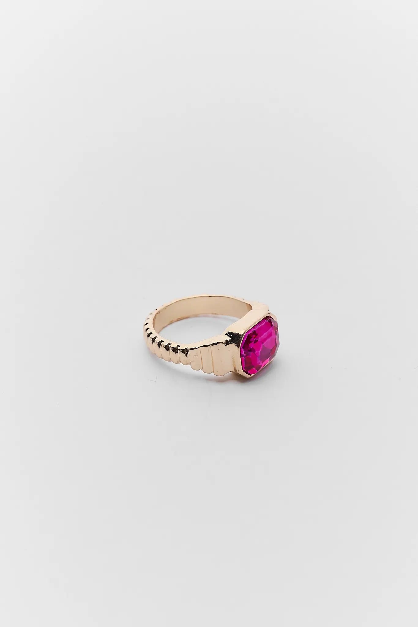 Gold ring with a pink gemstone on a light gray background