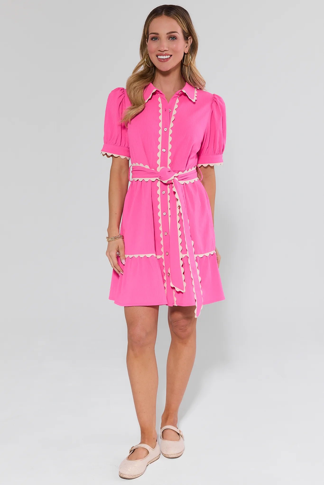 Woman wearing a pink dress with white trim on a light gray background