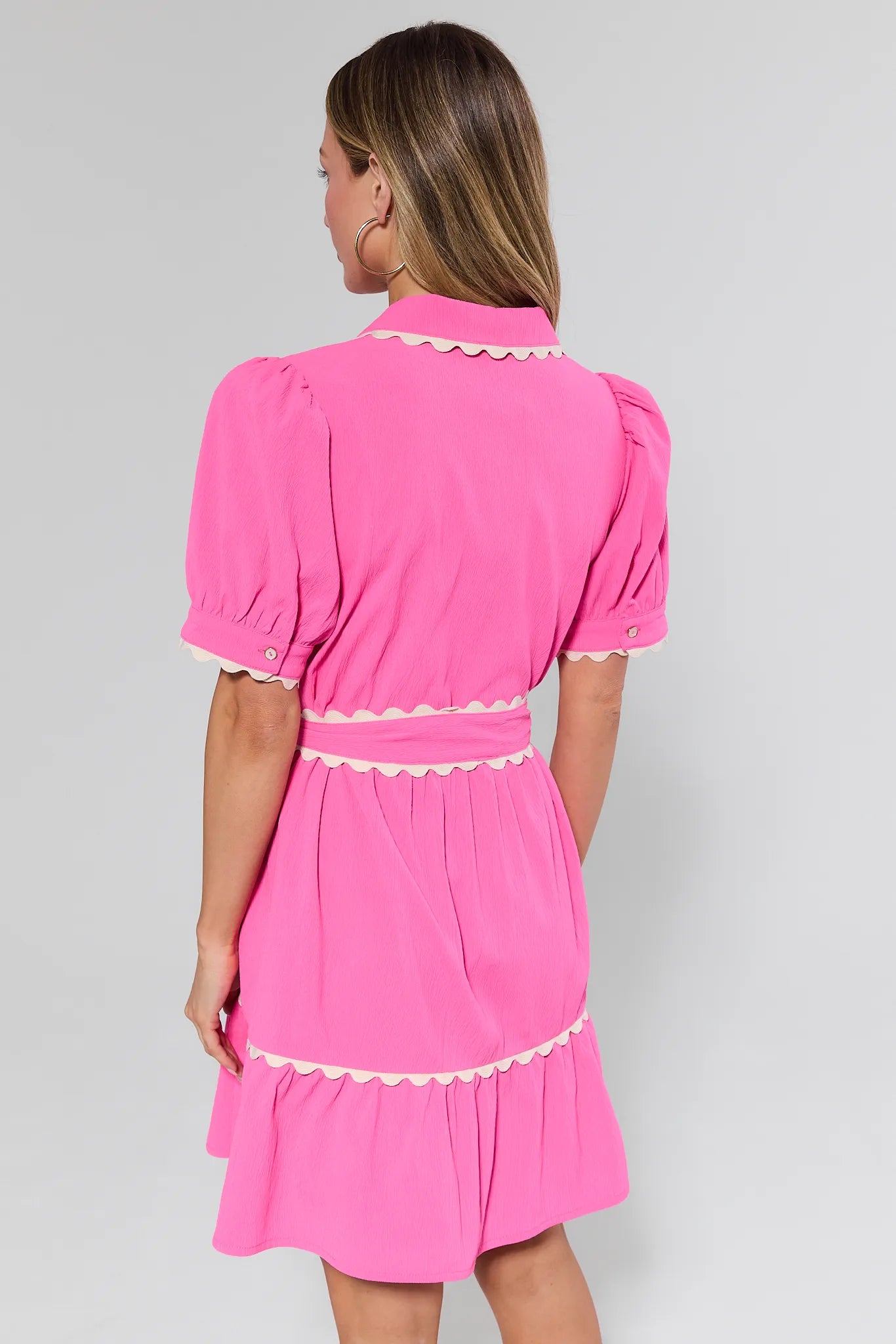 Woman wearing a pink dress with white trim on a gray background