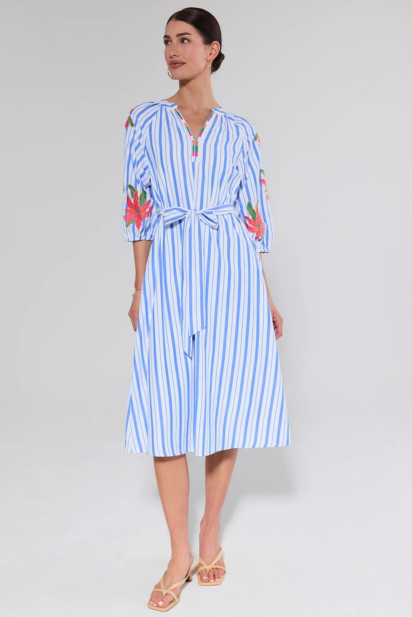 Woman wearing a blue and white striped dress with floral embroidery on a plain background