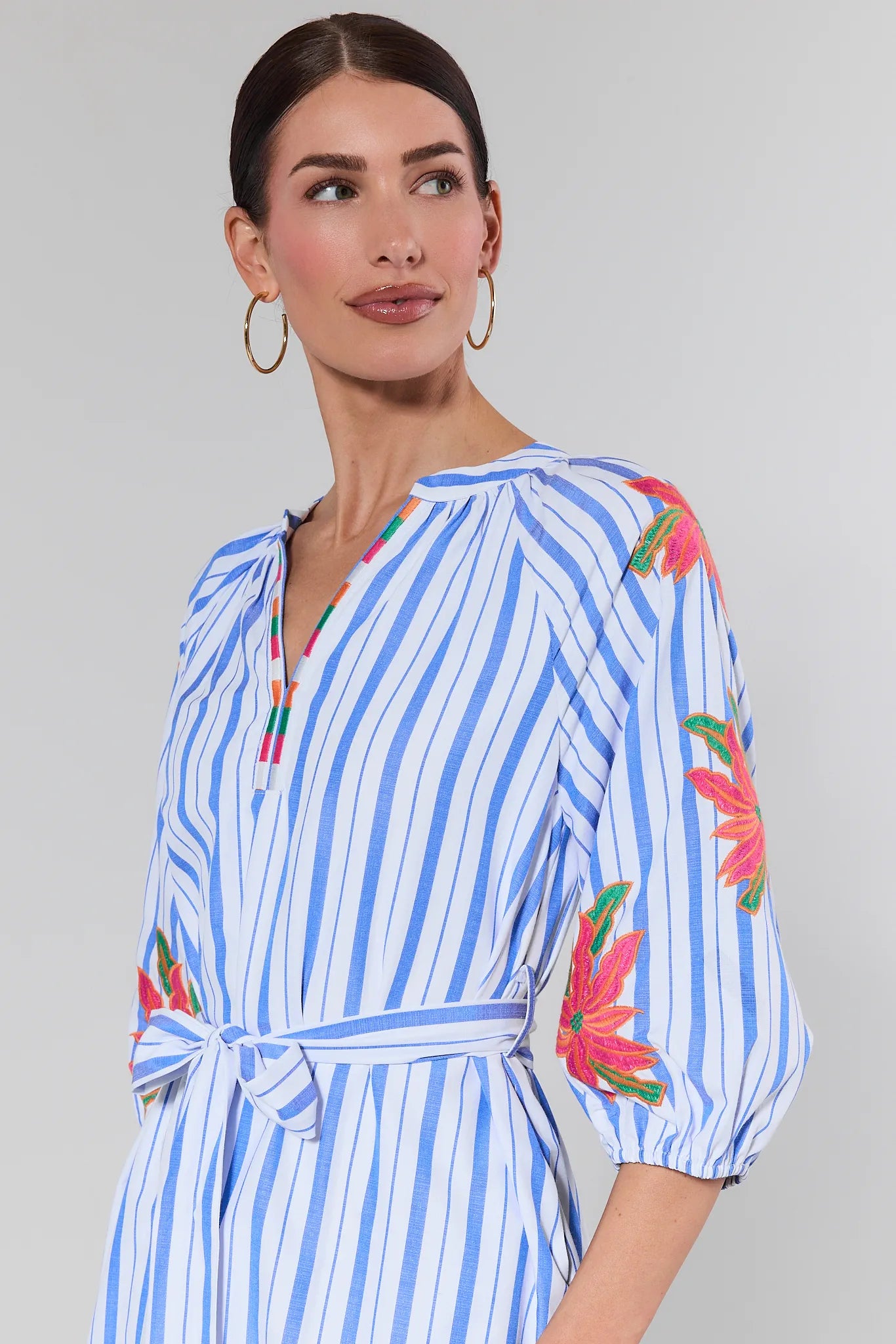 Woman wearing a blue and white striped dress with floral patterns on a gray background