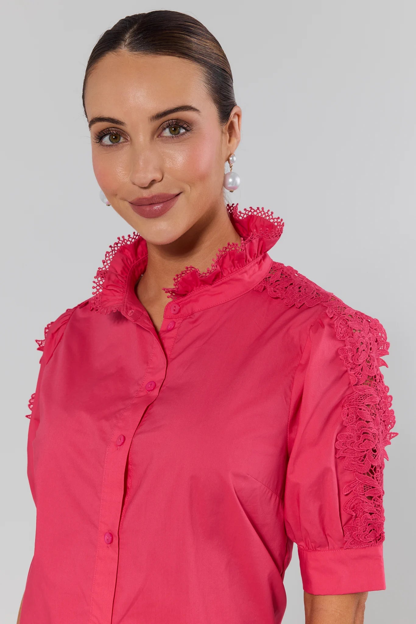 Woman wearing a pink blouse with lace details on a plain background
