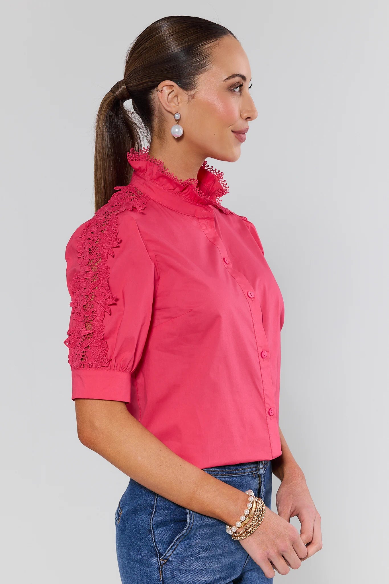 Woman wearing a pink blouse with lace details on a gray background