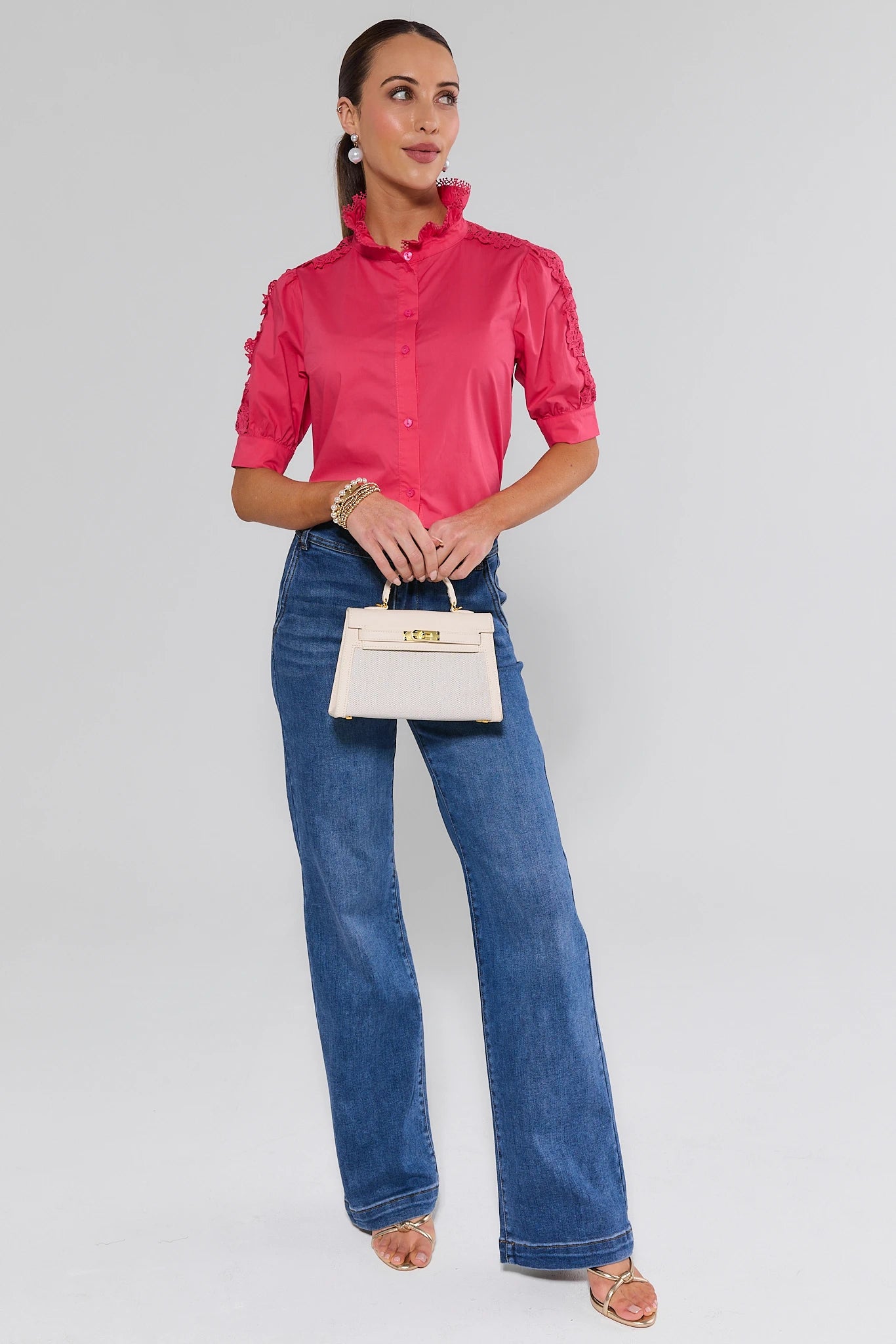 Woman wearing a pink blouse and blue jeans holding a white handbag on a gray background