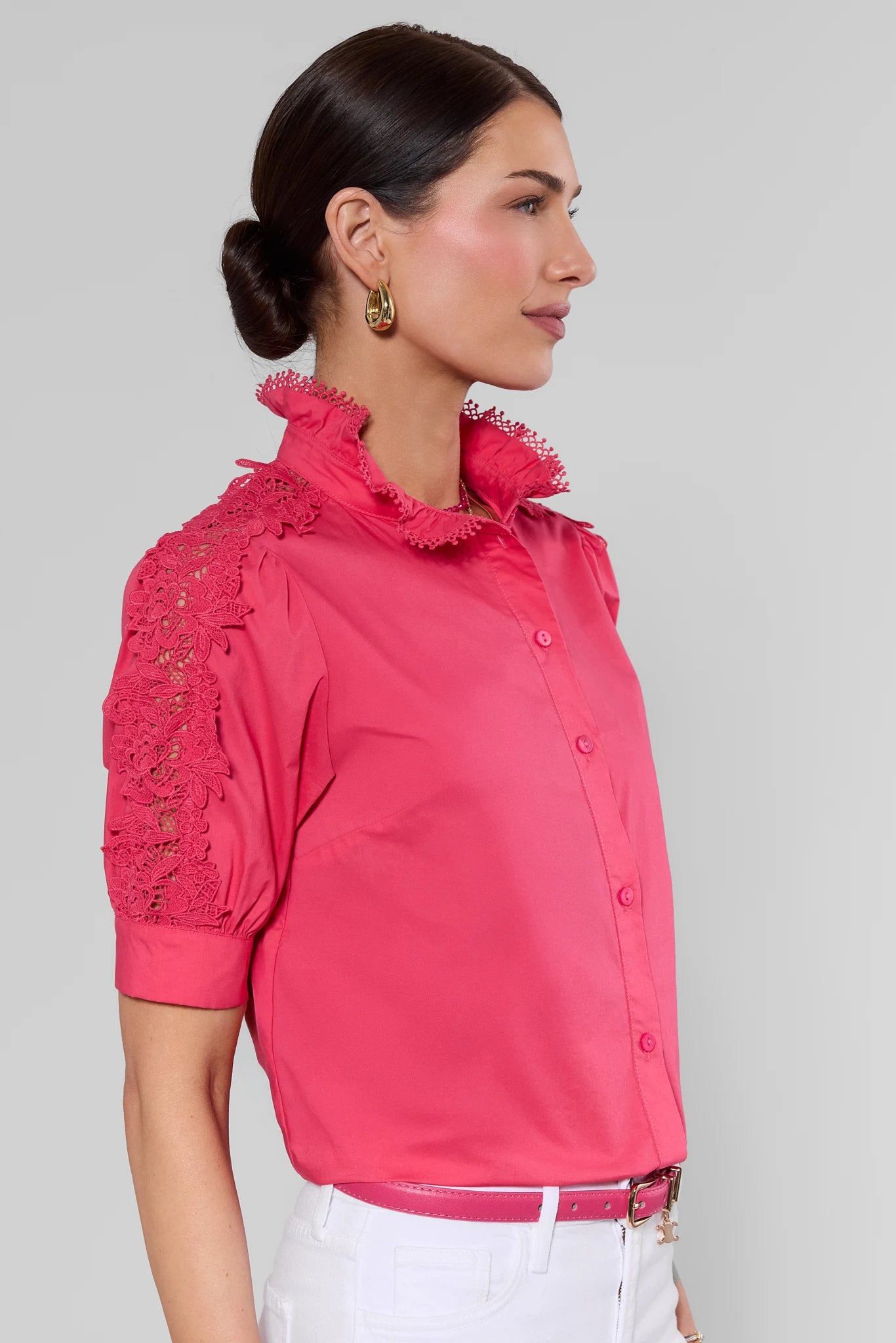 Woman wearing a pink blouse with lace details on a gray background