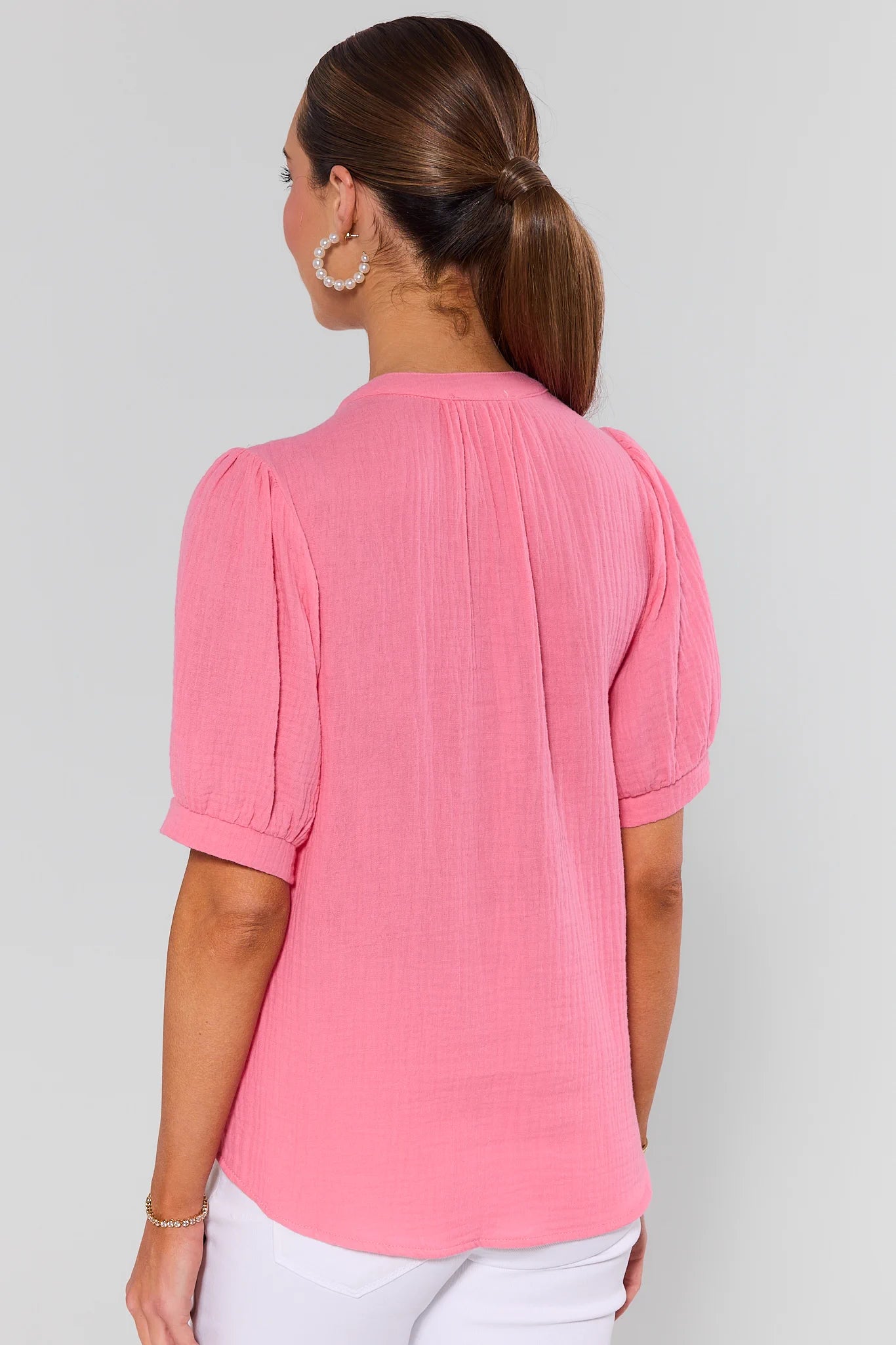 Woman wearing a pink blouse with short sleeves on a plain background