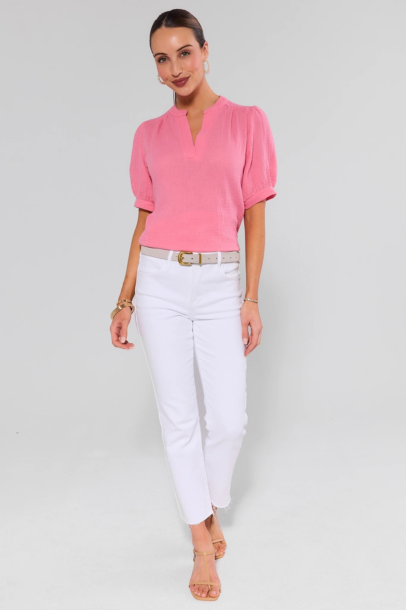 Woman wearing a pink blouse and white pants on a plain background