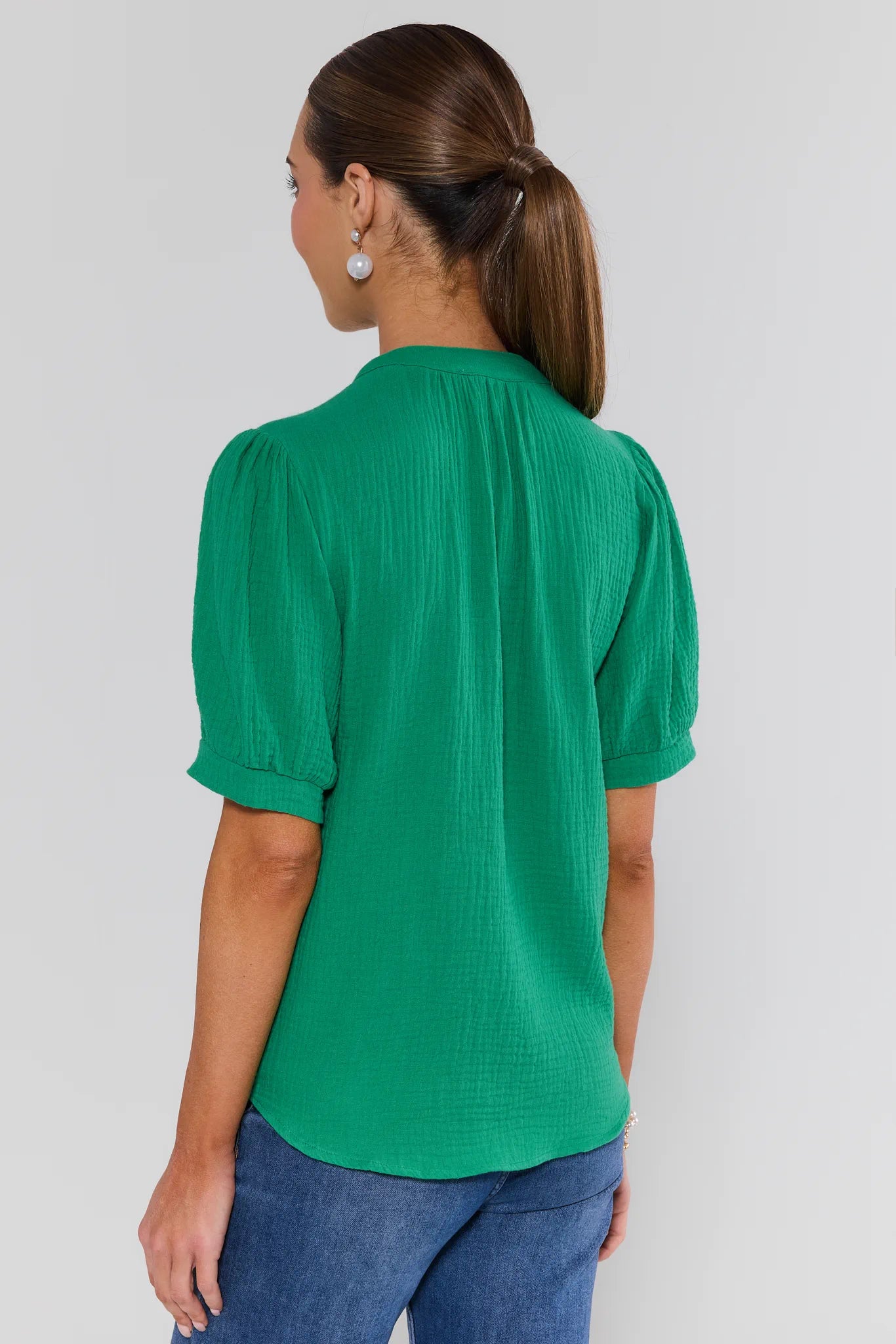 Woman wearing a green blouse with puffed sleeves on a plain background