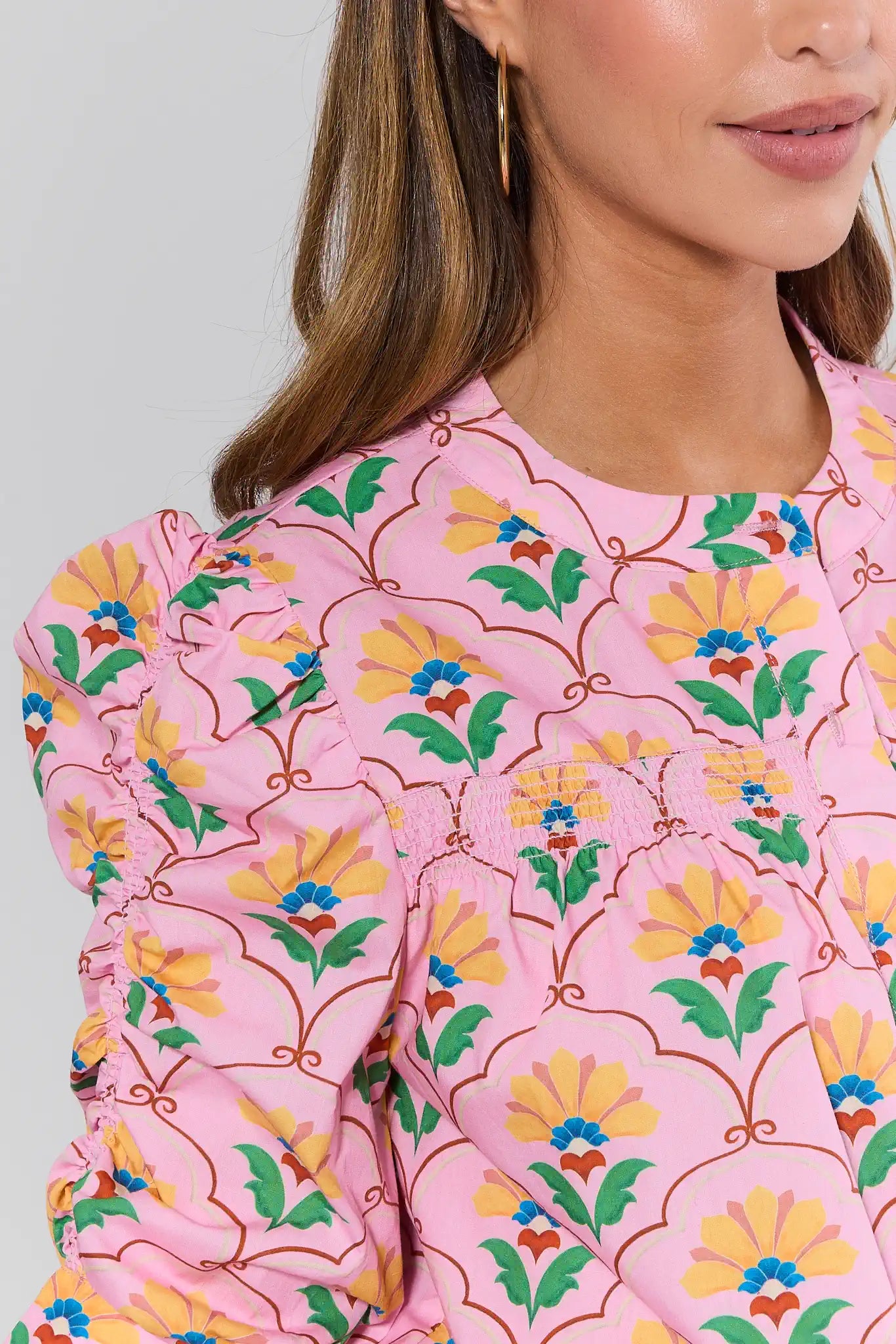 Woman wearing a pink floral blouse with colorful patterns on a plain background
