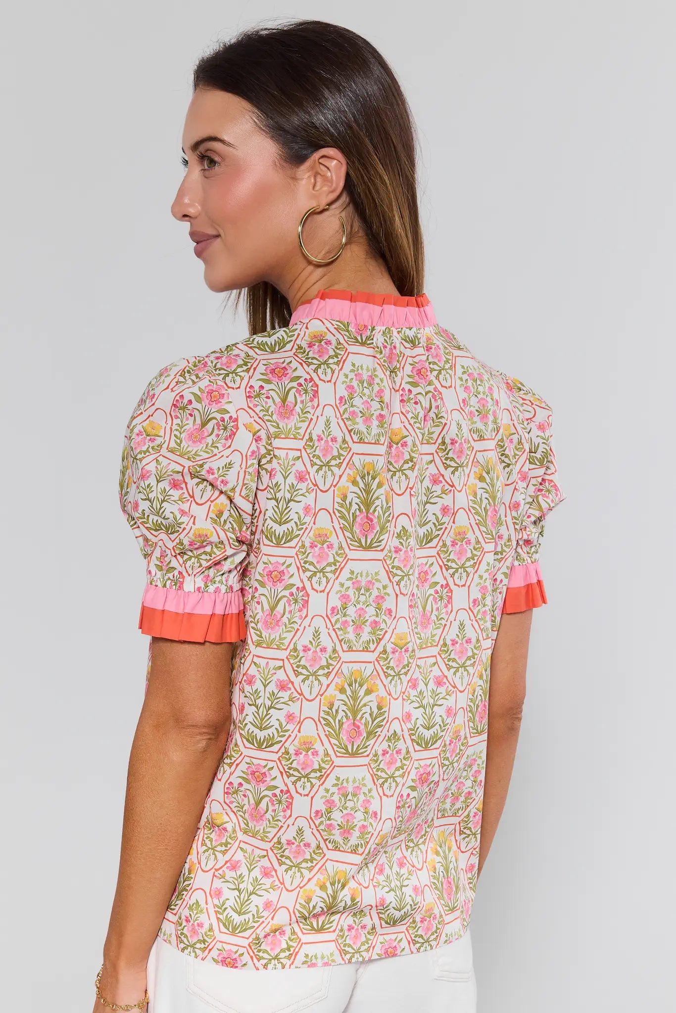 Woman wearing a patterned blouse with pink accents on a plain background