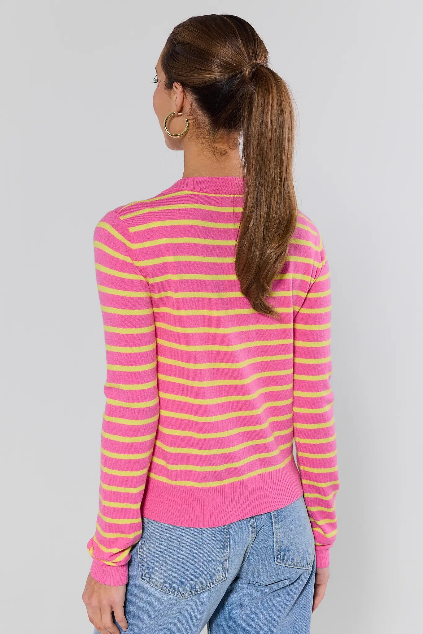 Woman wearing a pink and yellow striped sweater with blue jeans on a plain background