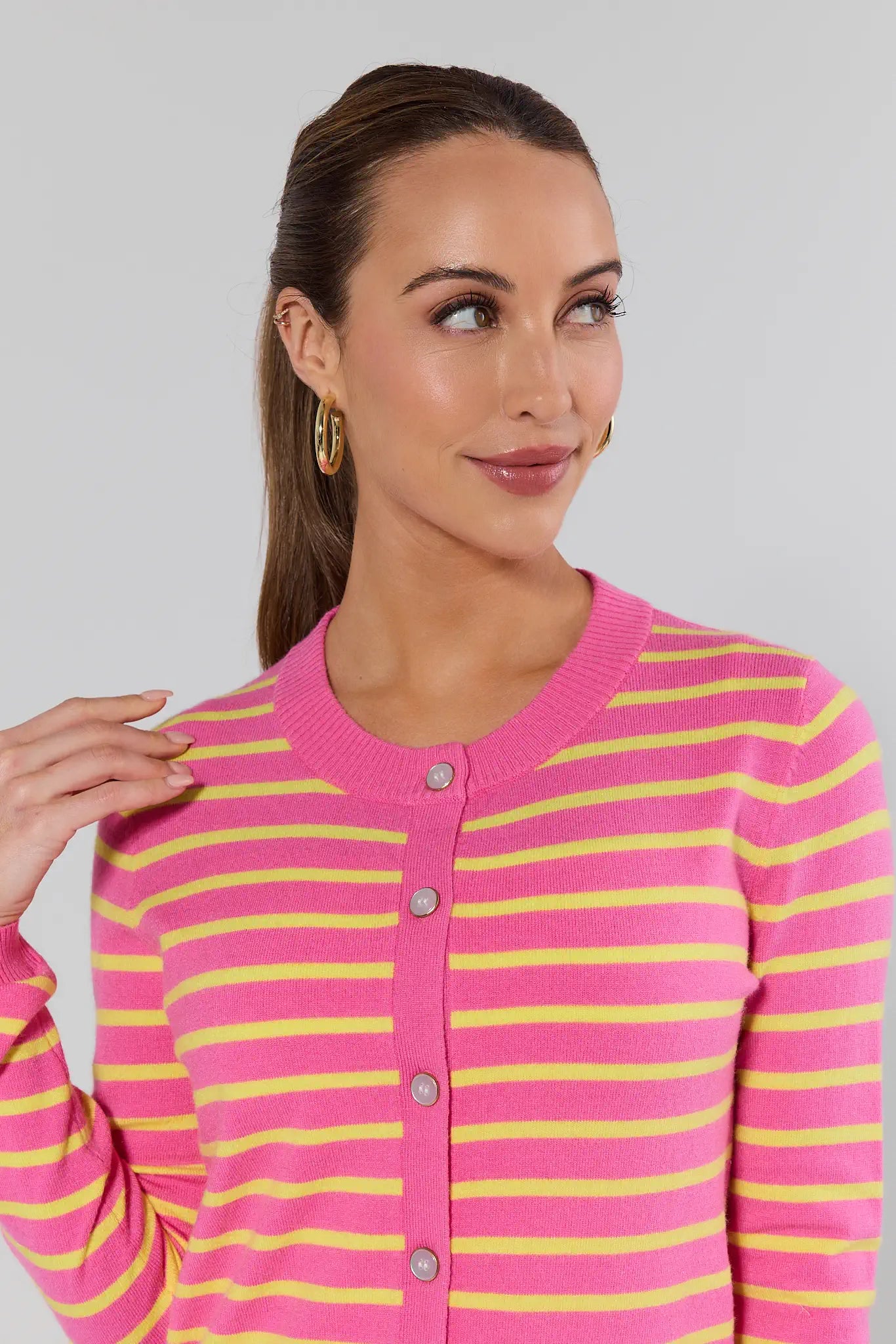 Woman wearing a pink and yellow striped cardigan against a plain background