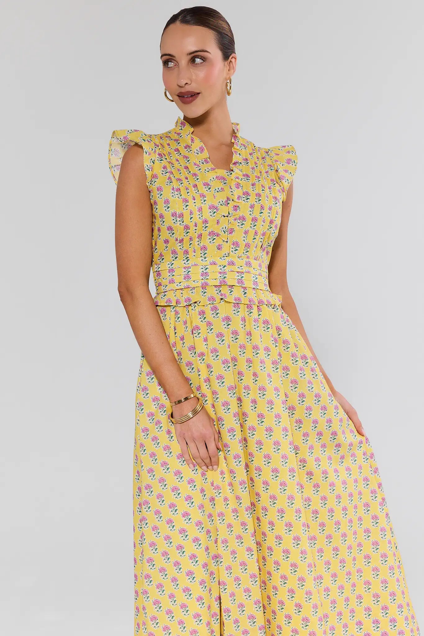 Woman wearing a yellow floral dress against a gray background