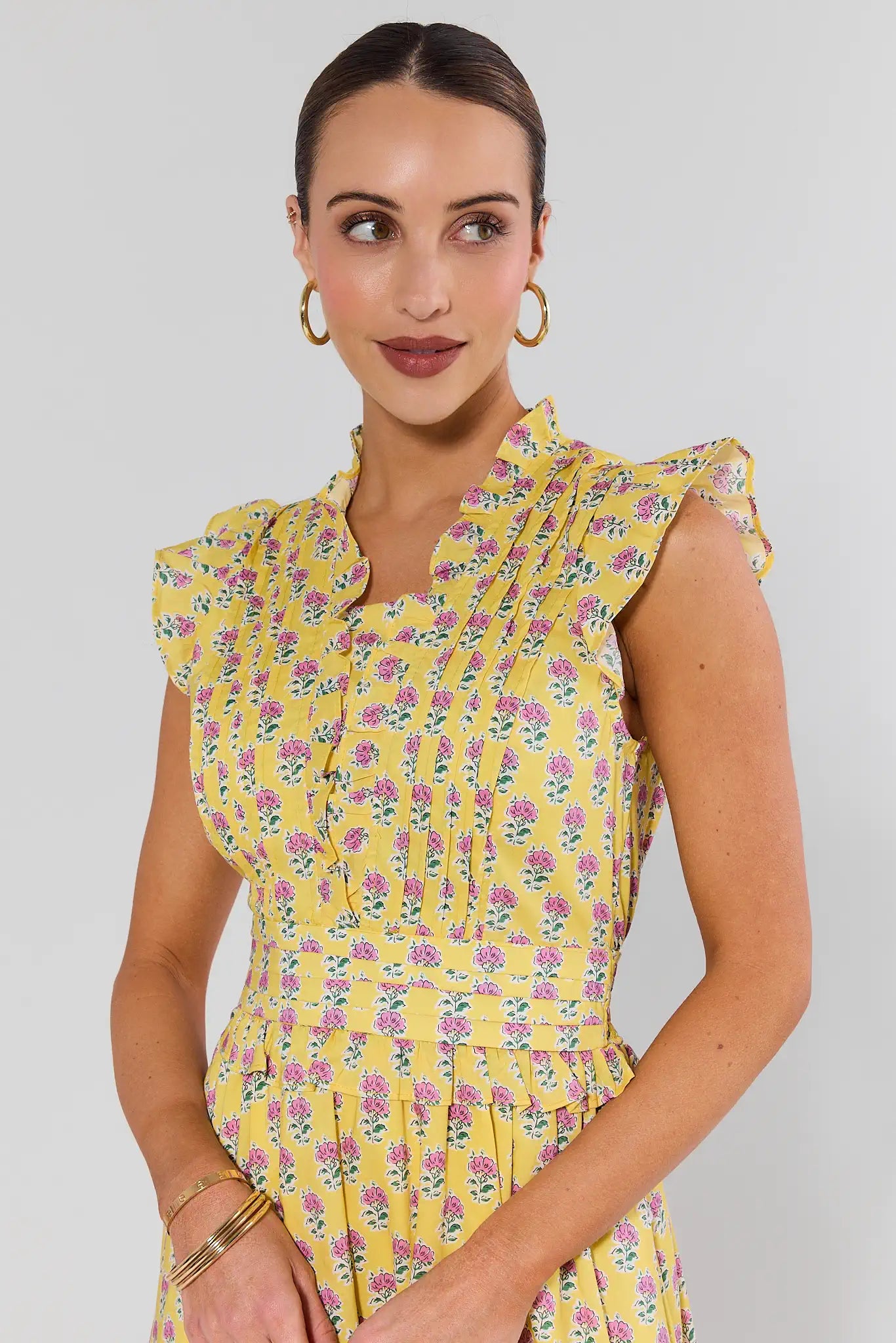 Woman wearing a yellow floral dress against a plain background