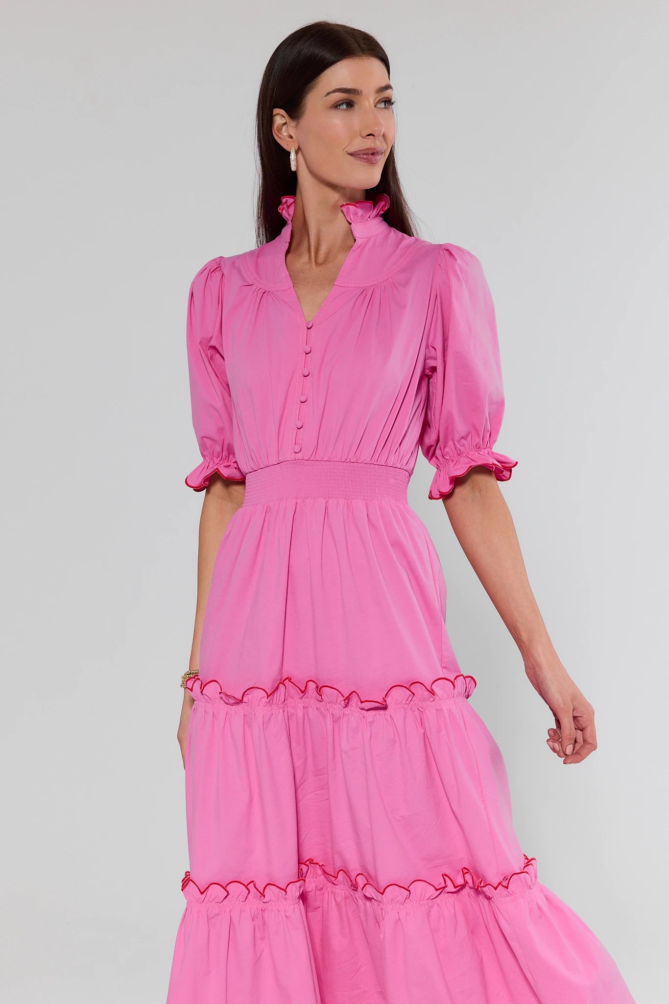 Woman wearing a pink dress with ruffled sleeves and bottom hem on a white background