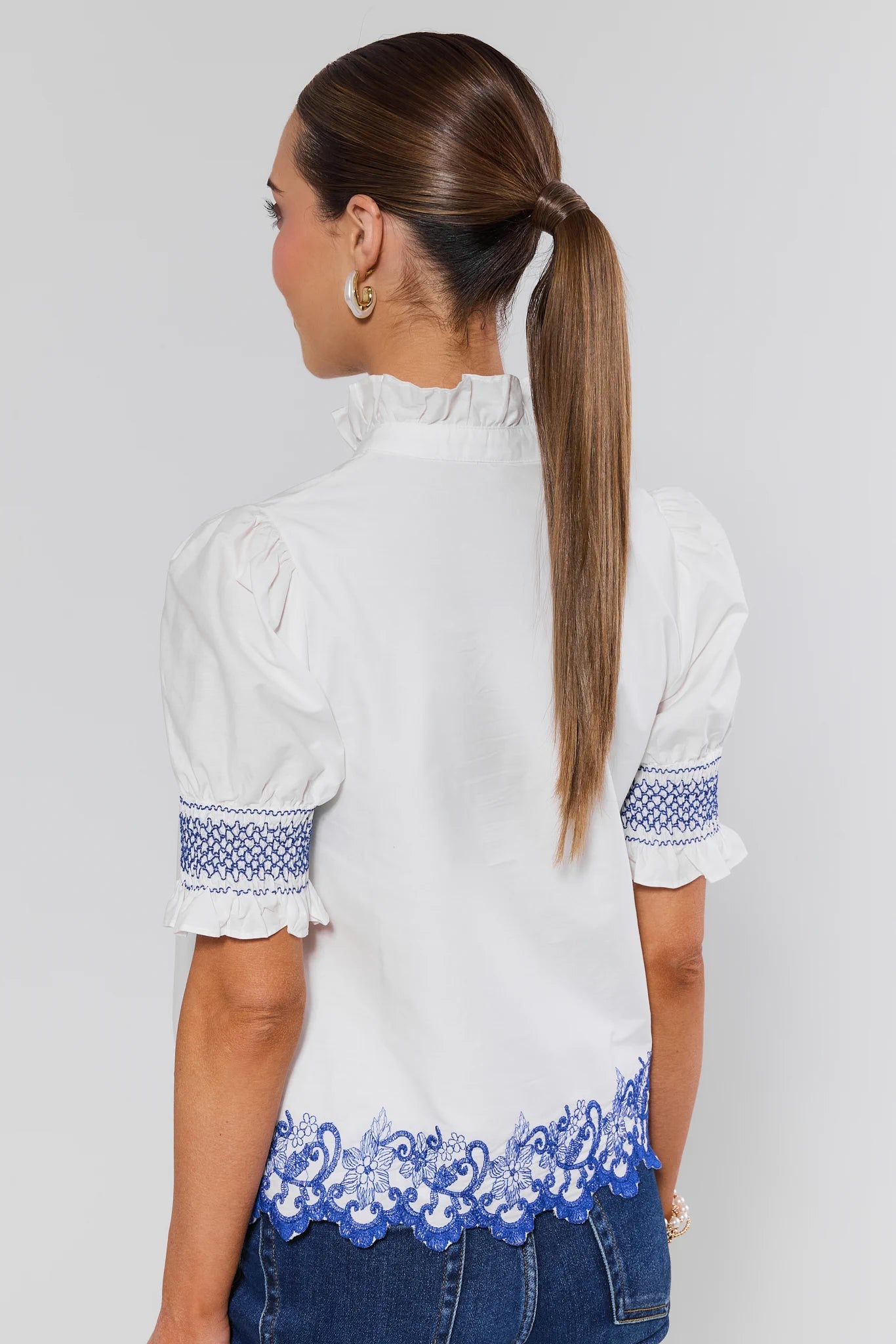 Woman wearing a white blouse with blue embroidery on a plain background