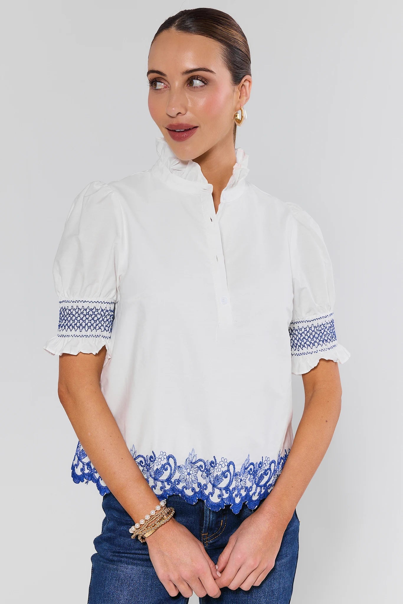 Woman wearing a white blouse with blue embroidery on a plain background