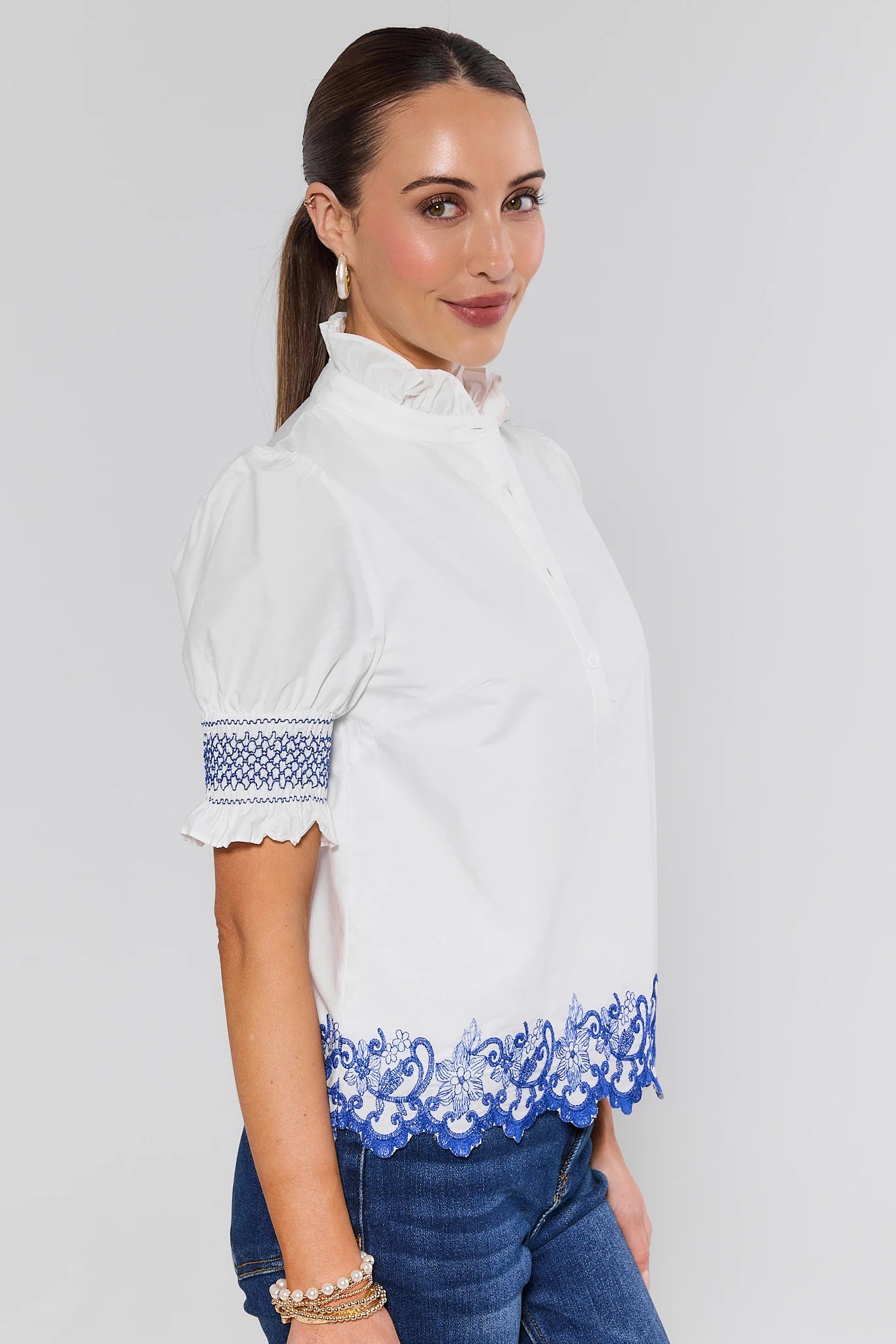 Woman wearing a white blouse with blue embroidery on a plain background