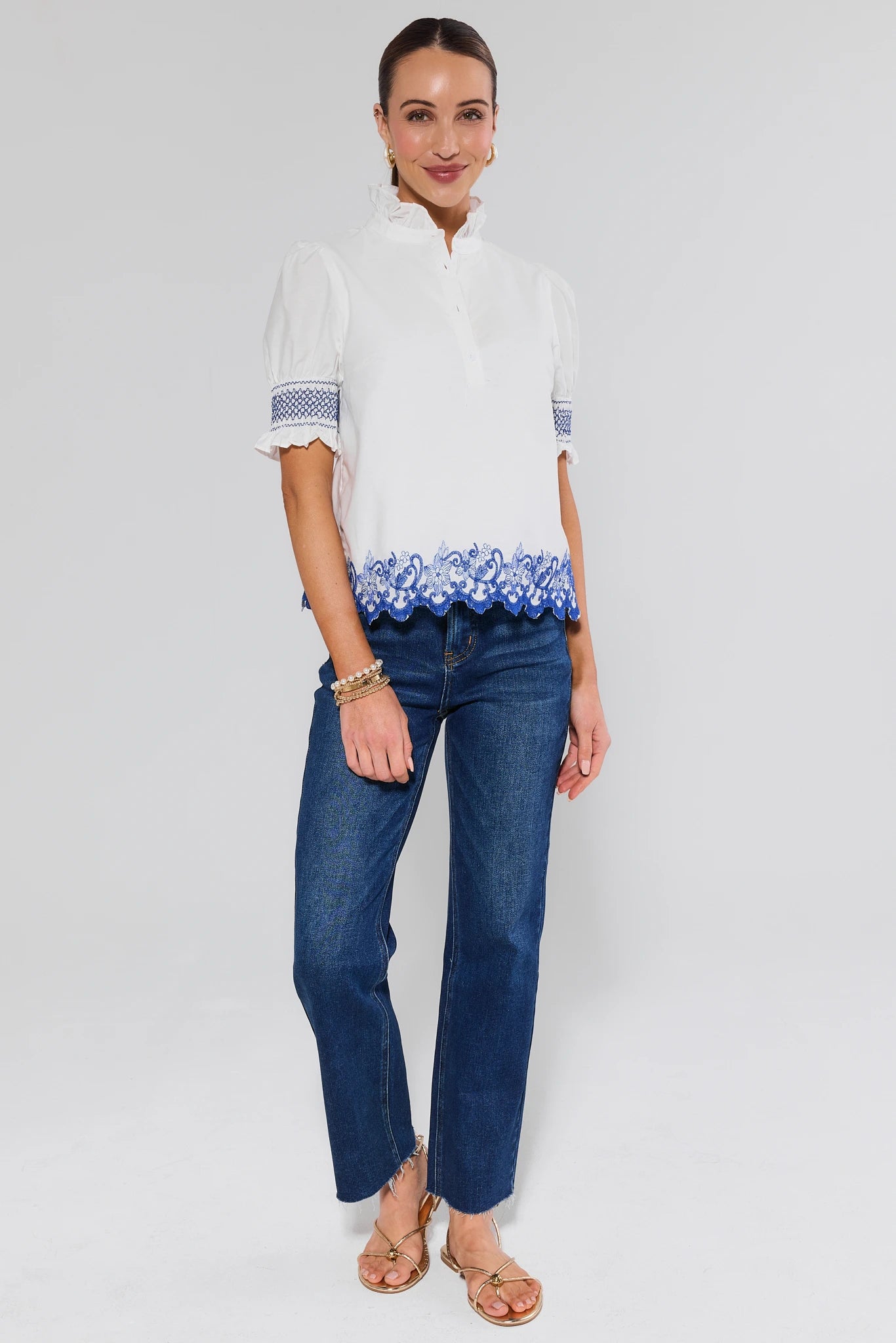 Woman wearing a white blouse with blue trim and blue jeans on a white background