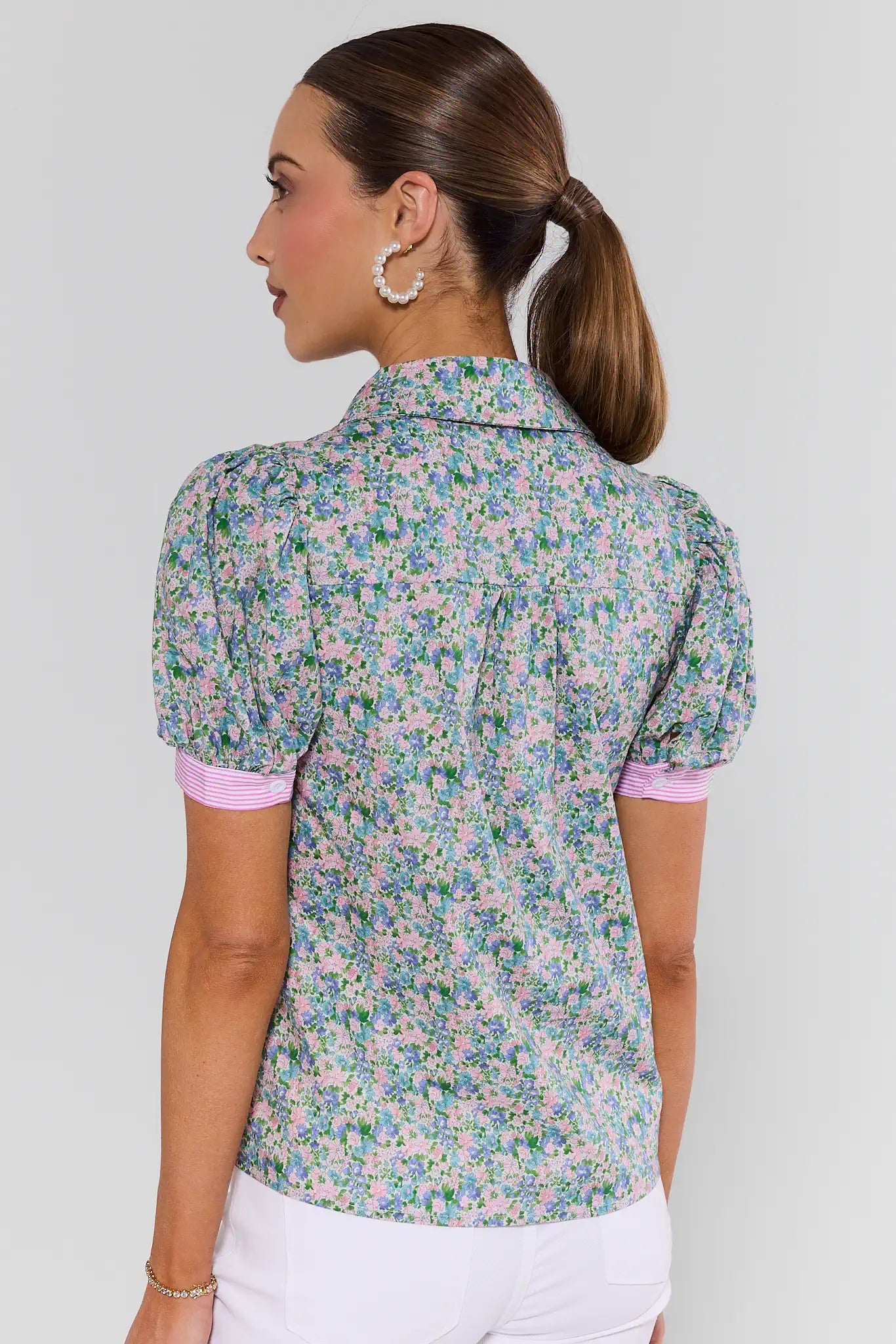 Woman wearing a floral blouse with pink trim on a plain background