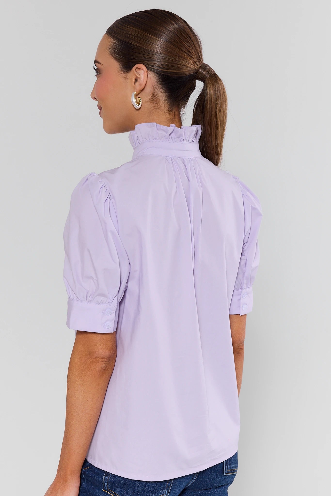 Woman wearing a light purple blouse with ruffled collar against a plain background